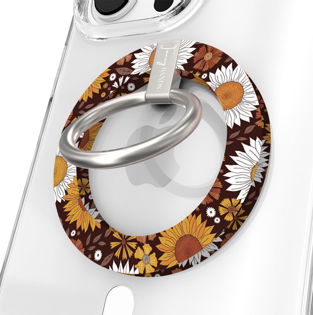 Harvest Sunflowers Hold It Fancy MagSafe grip ring close-up on a clear iPhone case, showing the chocolate brown base packed with retro sunflowers and white daisies around the silver rotating ring.