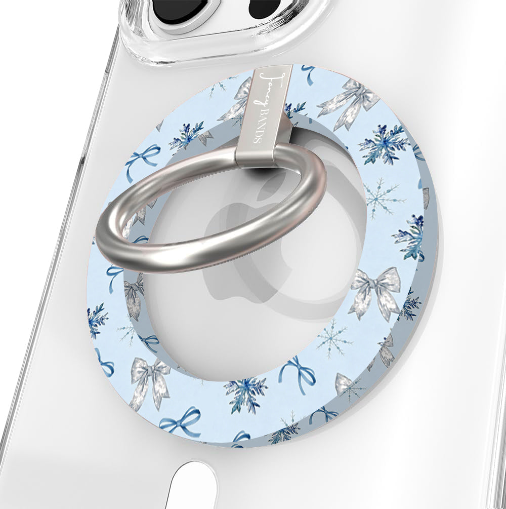 Close-up of the Snow Pretty In Blue MagSafe grip ring with silver bows and navy snowflakes on powder blue and a brushed silver ring on a clear iPhone case