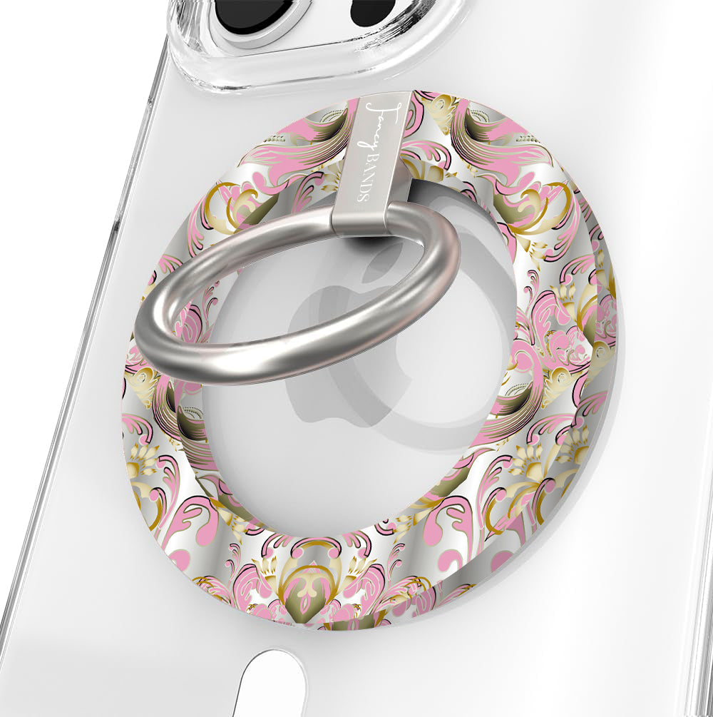 The Pink Heiress Hold It Fancy MagSafe grip ring on a clear iPhone case, pink and gold baroque scrollwork on pearl white around the silver rotating ring.