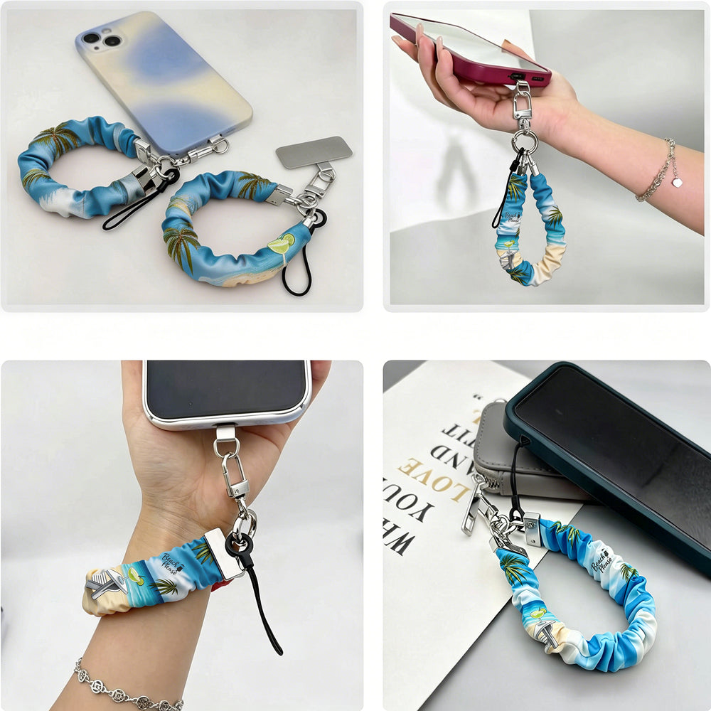 Blue and green satin Beach Please scrunchie phone wrist strap clipped to the matching Beach Please Wavy Luxe iPhone case with a beach chair and cocktail design, styled on a sandy shoreline background with starfish and ocean waves.