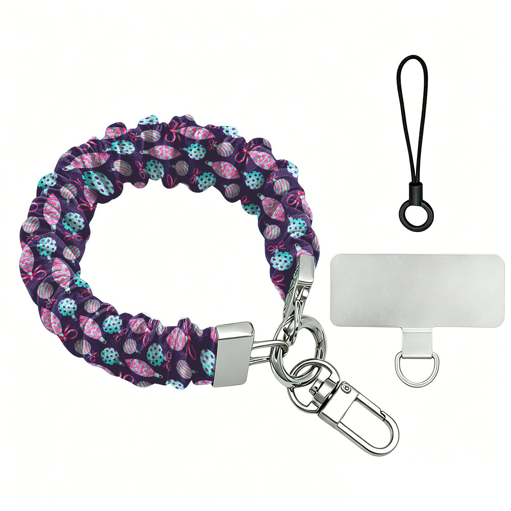 Just One More Ornament scrunchie phone wrist strap laid flat with silver clasp and phone tab, pink and aqua ornaments on plum