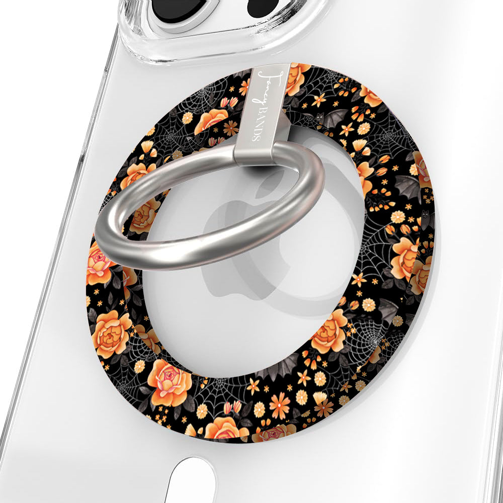 Haunted Blossoms Hold It Fancy MagSafe grip ring close-up on a clear iPhone case, showing the black ring with burnt-orange roses, mushrooms and gold spiderwebs around the silver rotating ring.