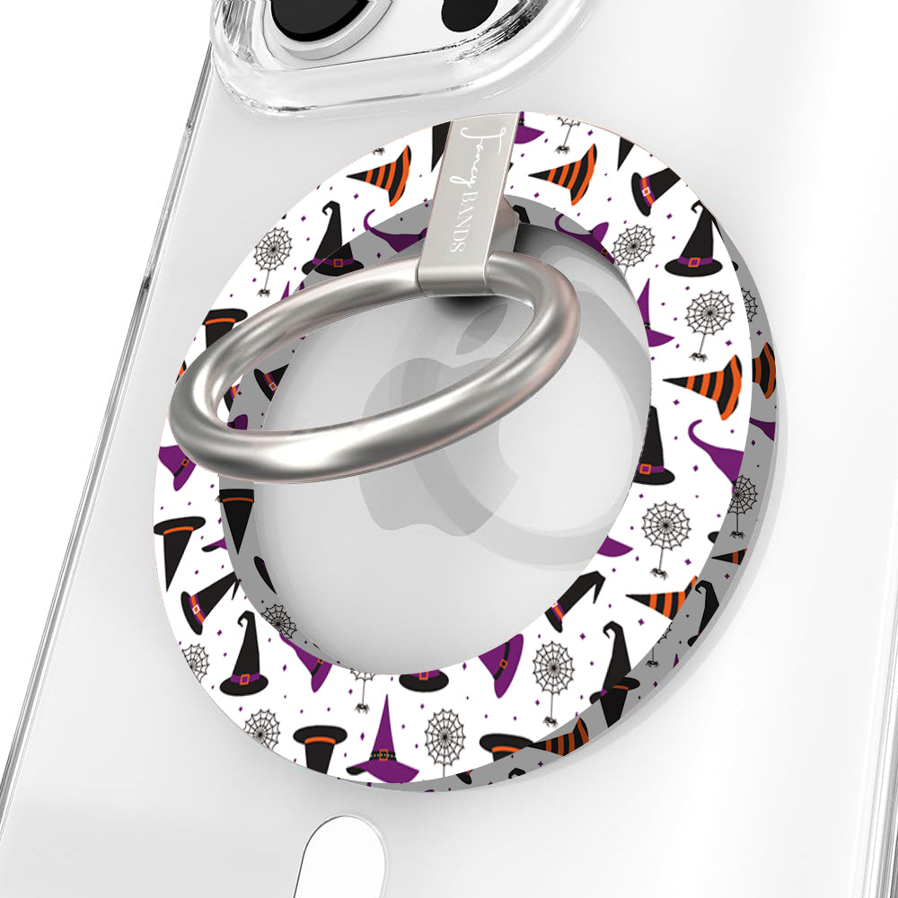 Witch Please Hold It Fancy MagSafe grip ring close-up on a clear iPhone case, showing the white ring scattered with purple, black and striped orange witch hats around the silver rotating ring.