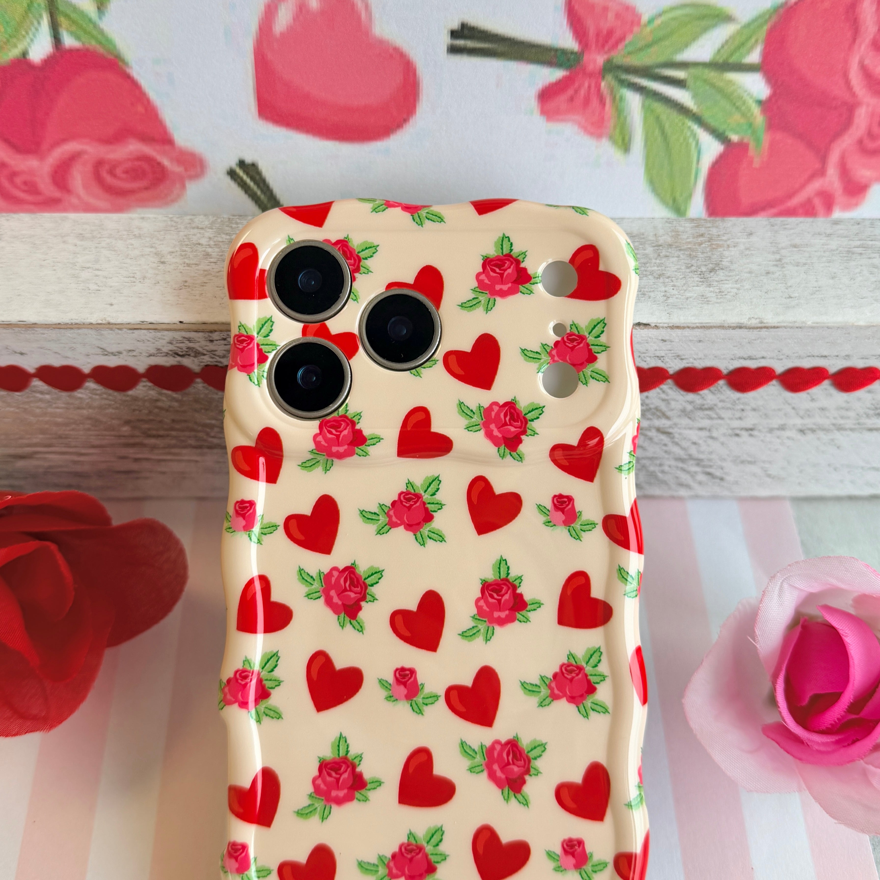 Cream colored wavy iPhone case featuring a pattern of red hearts and small pink roses with green leaves.