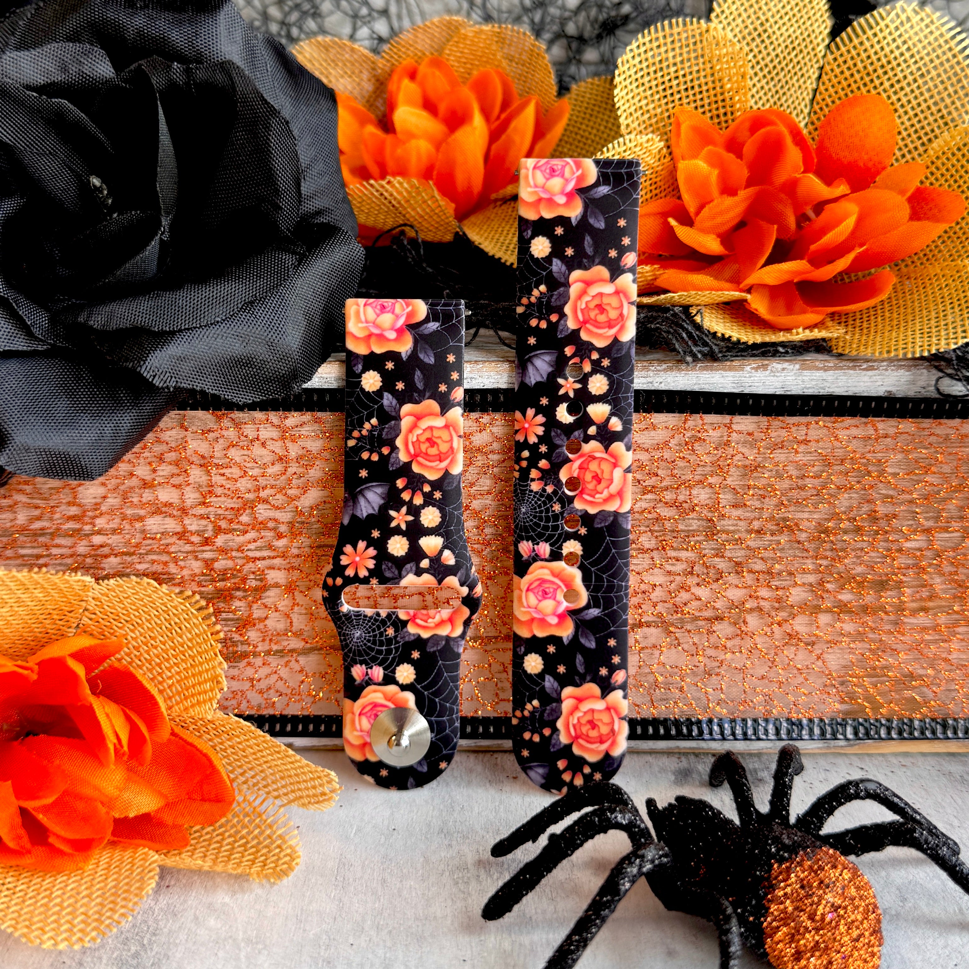 Two Haunted Blossoms Samsung Galaxy Watch band straps standing with black glitter spider props below the coral rose print.