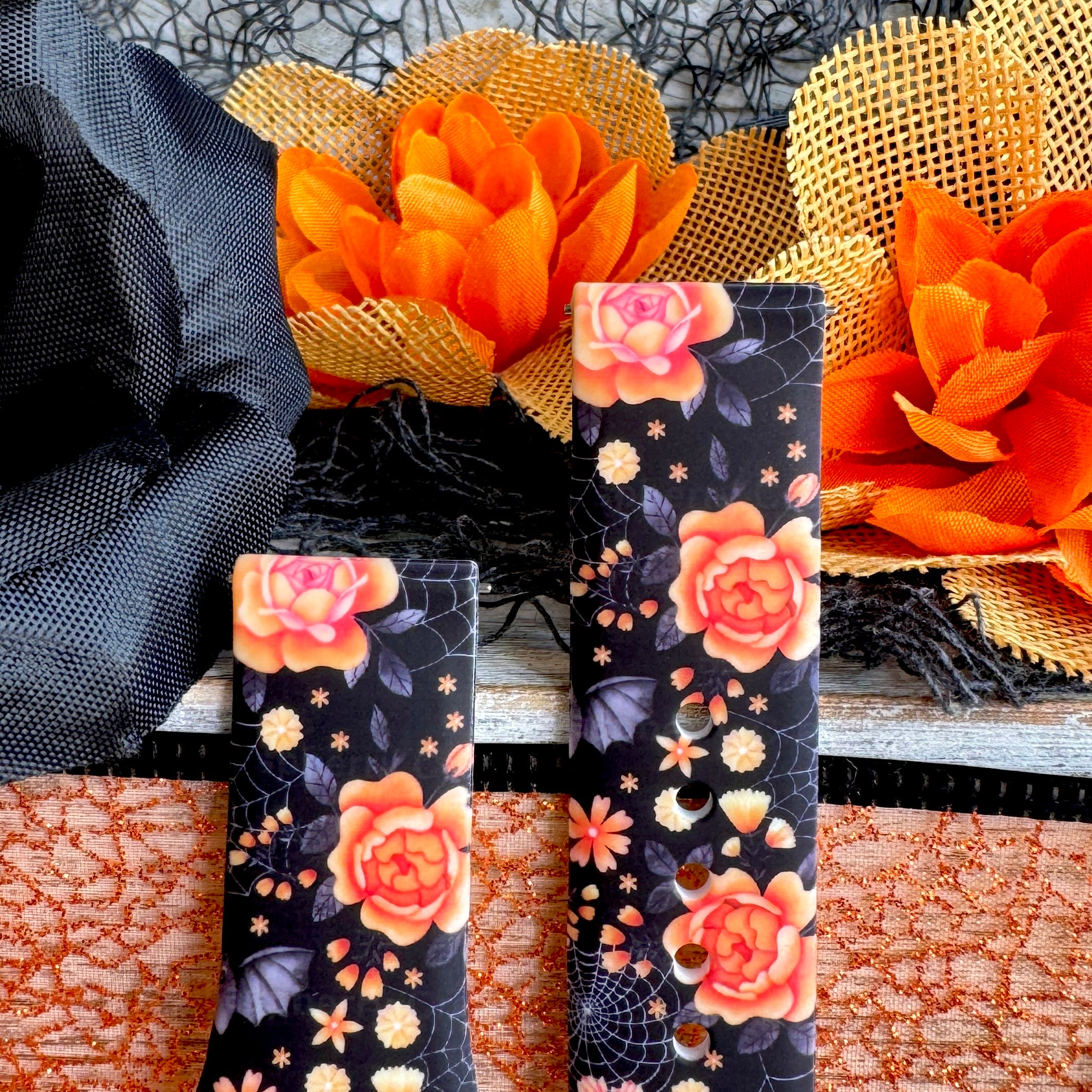 Haunted Blossoms Samsung Galaxy Watch band shown as two strap halves standing side by side against orange autumn blooms.