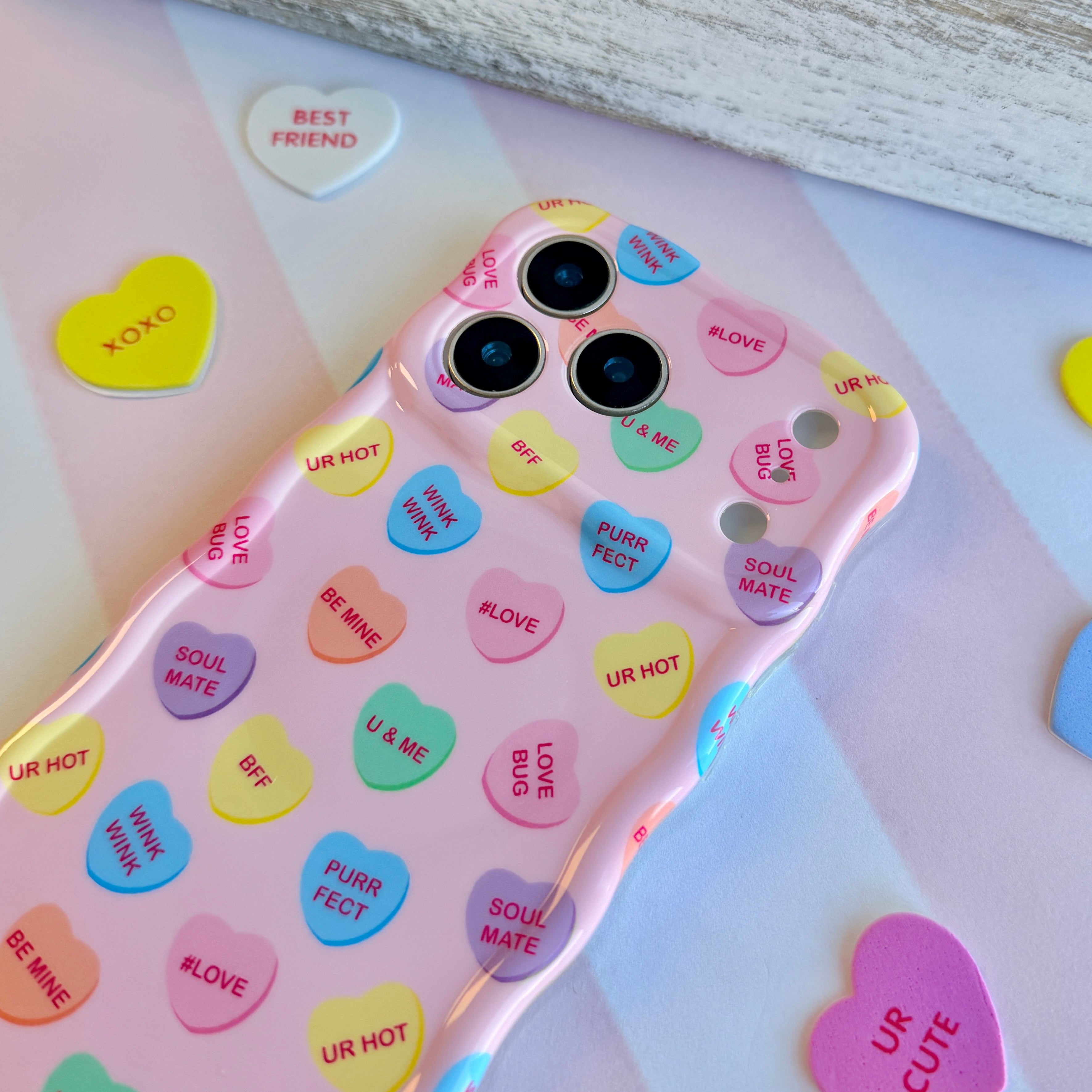 Pink wavy iPhone case featuring colorful candy conversation hearts with text like Be Mine, Ur Hot, and Soul Mate.