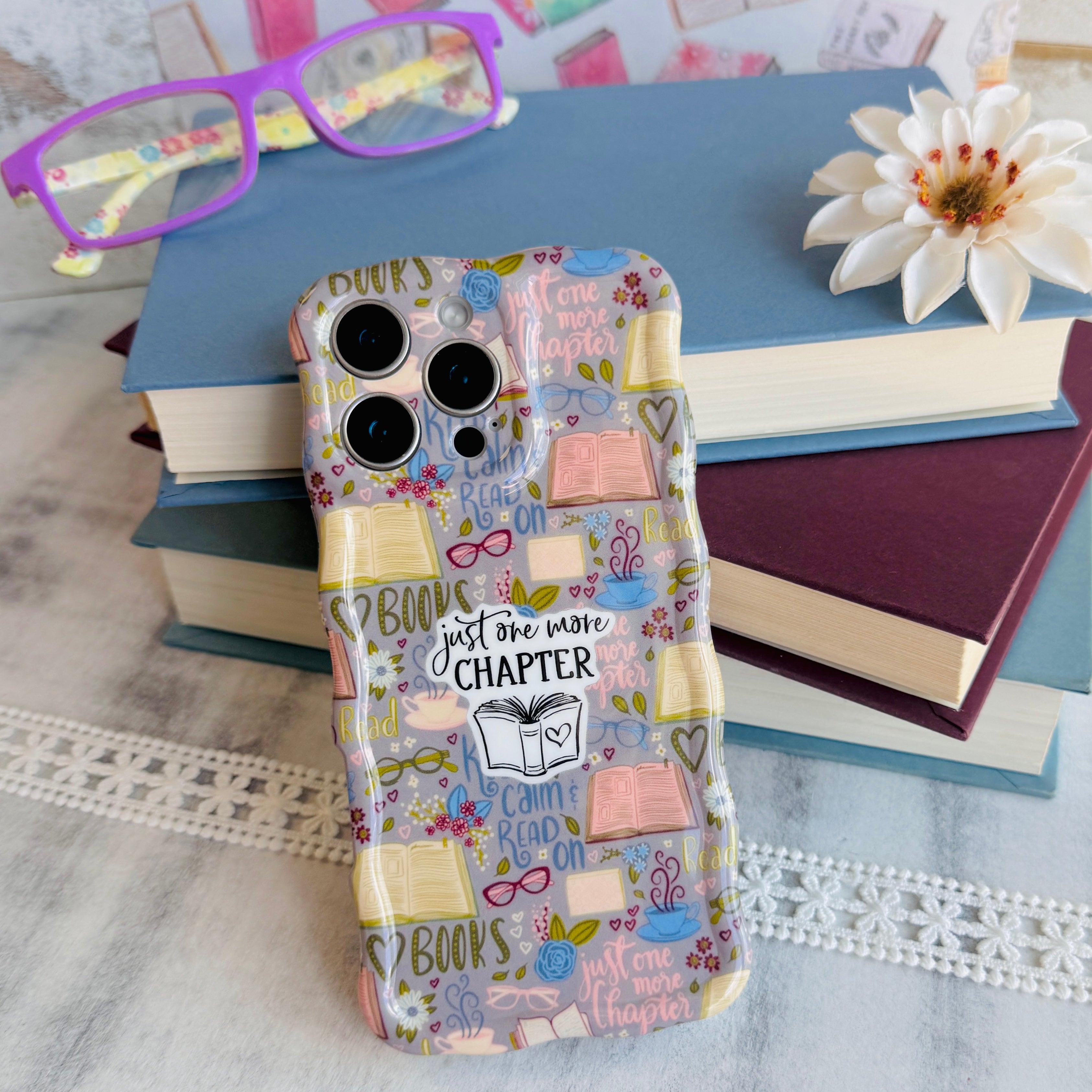 Phone case with book-themed design on a surface with books and glasses