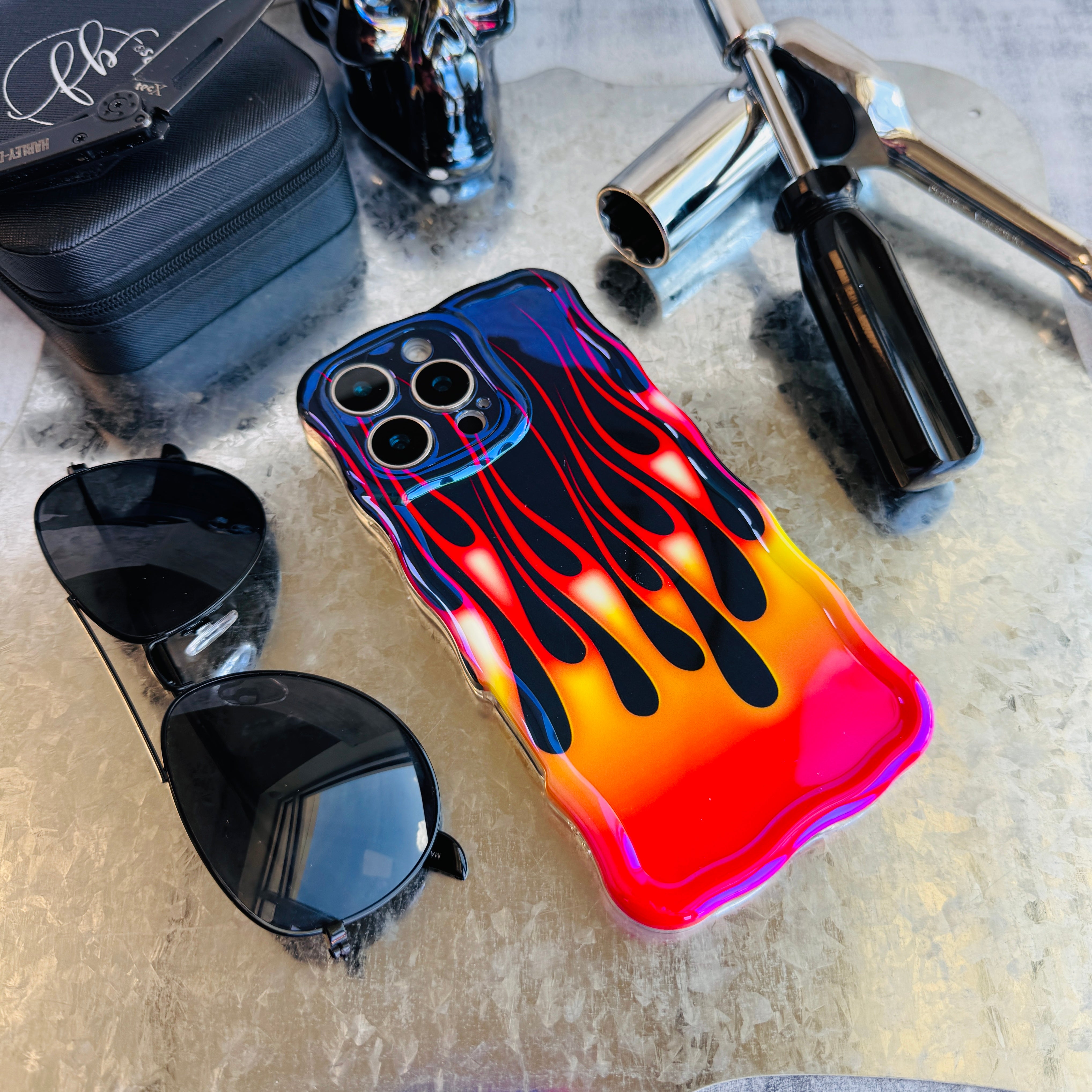 Phone case with flame design, sunglasses, and motorcycle parts on a textured surface