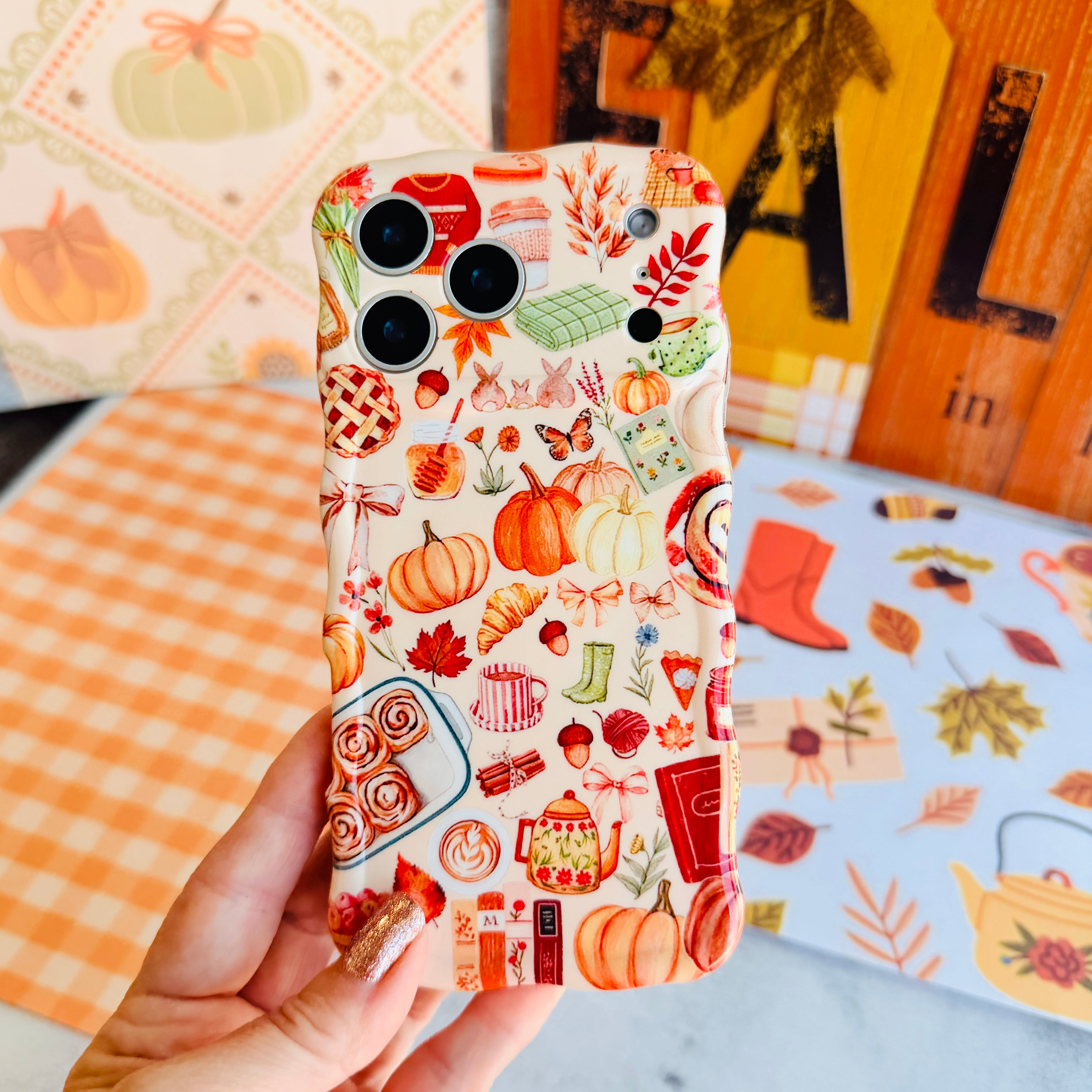 Hand holding the All The Fall Things Wavy Luxe MagSafe iPhone case with the matching grip ring attached, showing the cream watercolor pumpkin, pie and cinnamon roll collage.