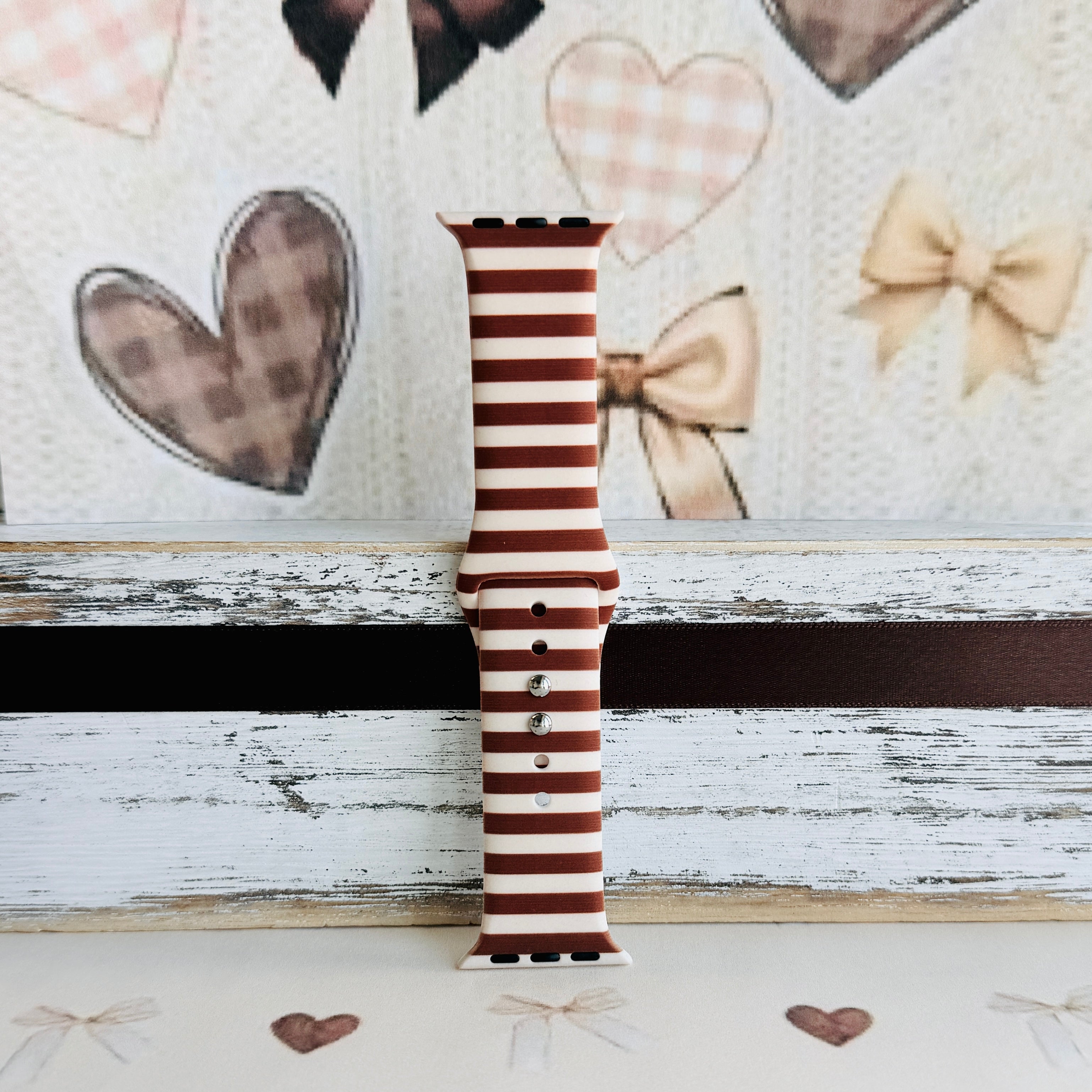 Sweet Espresso Stripes Apple Watch band single strap half standing against a plaid heart and bow backdrop, showing the espresso and cream stripe print.