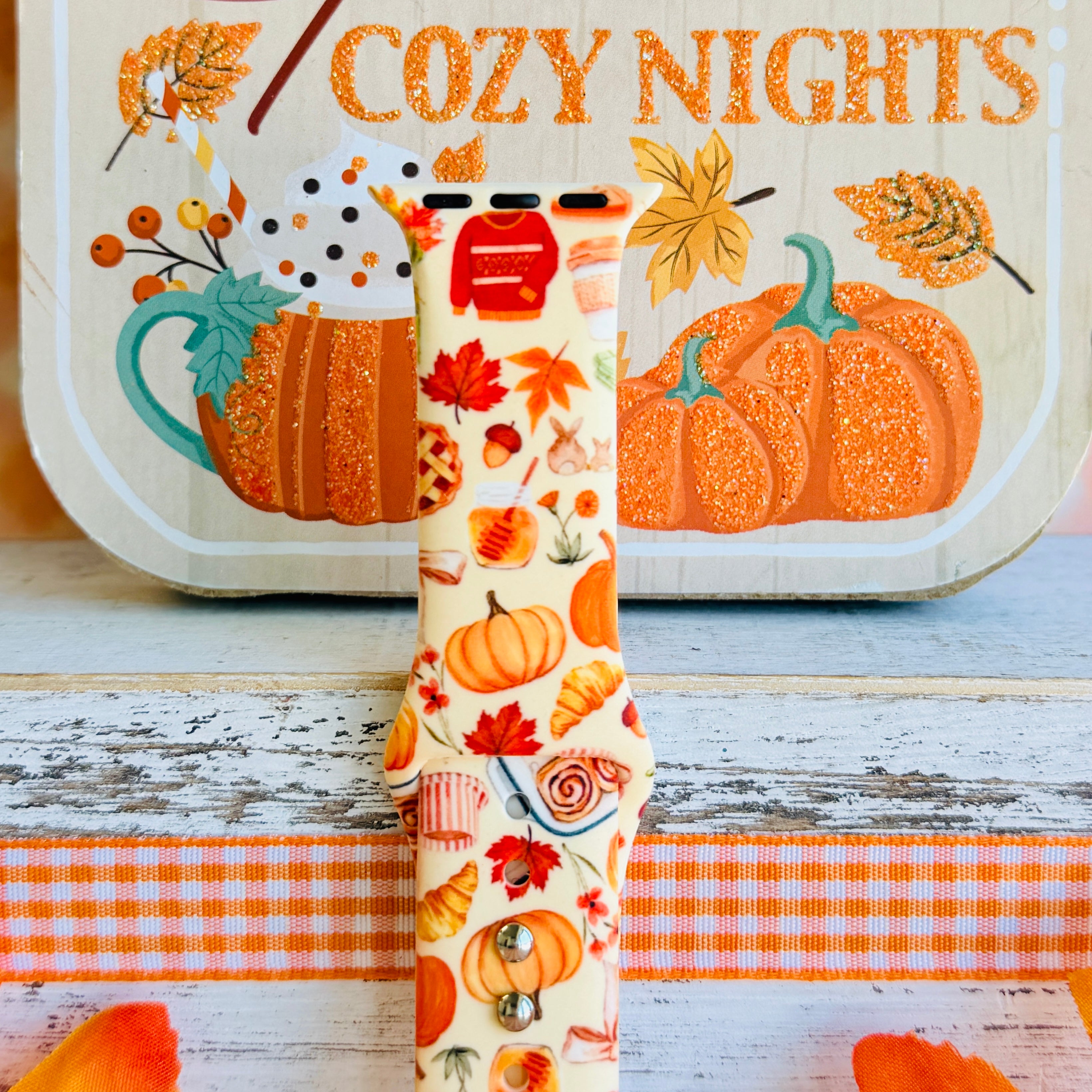 Close-up of the All The Fall Things Apple Watch band showing the watercolor detail on individual pumpkins, coffee cups and cinnamon rolls across the cream strap.