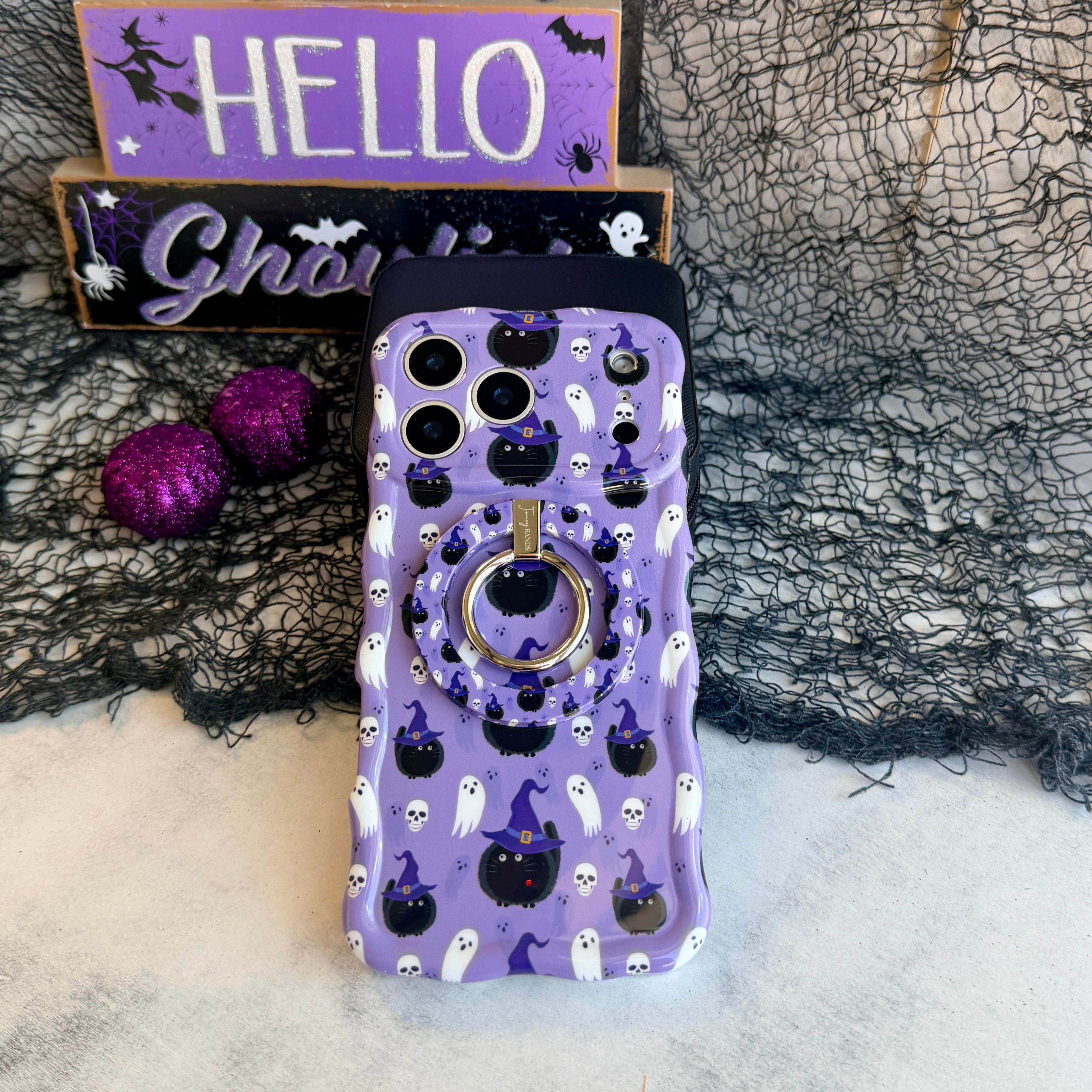 Ghostly Whisker's MagSafe grip ring attached to the matching lavender Wavy Luxe case, shown on black spiderweb mesh with a HELLO Ghoulies sign.