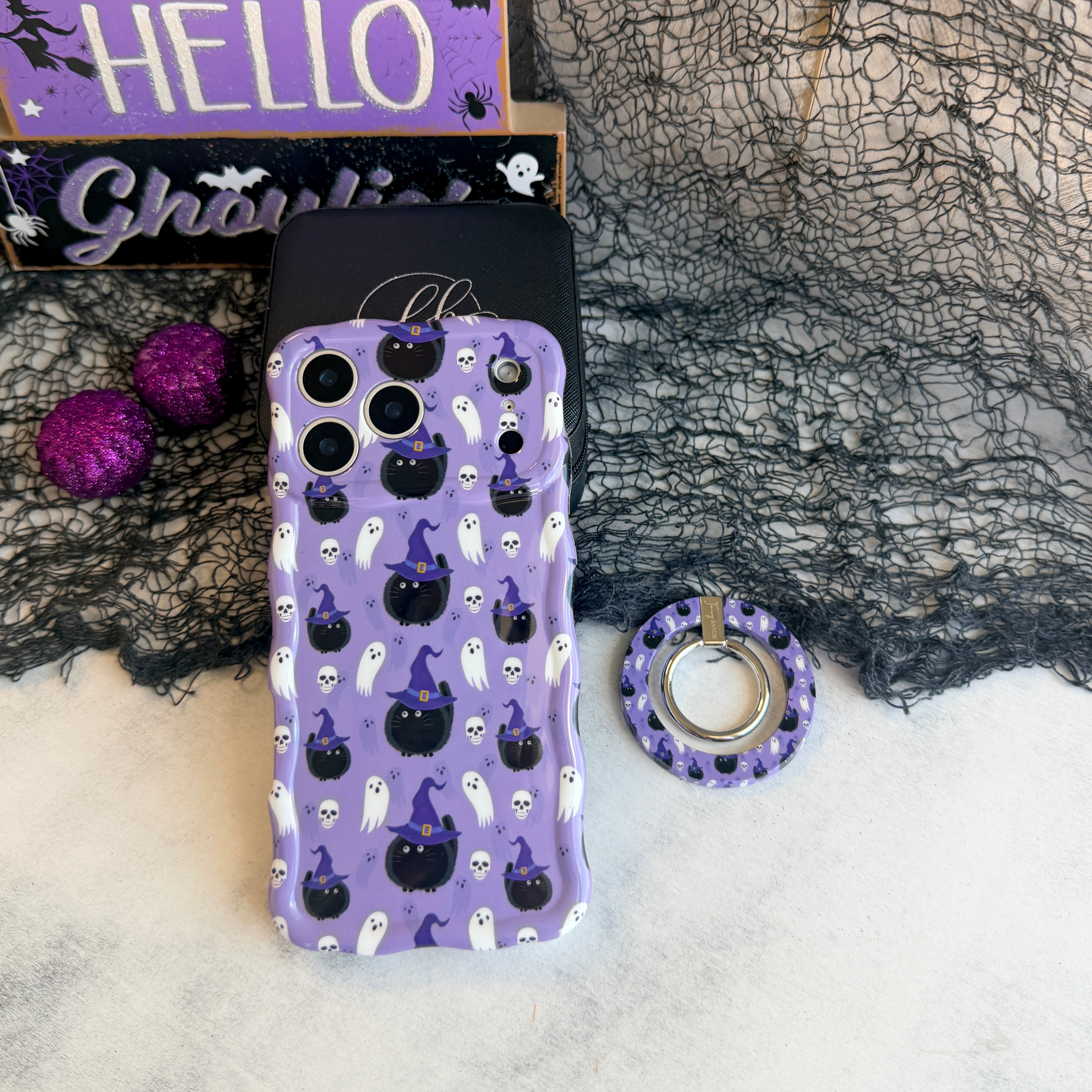 Ghostly Whisker's MagSafe grip ring lying beside the matching lavender ghost and cat Wavy Luxe case with purple glitter pumpkins.