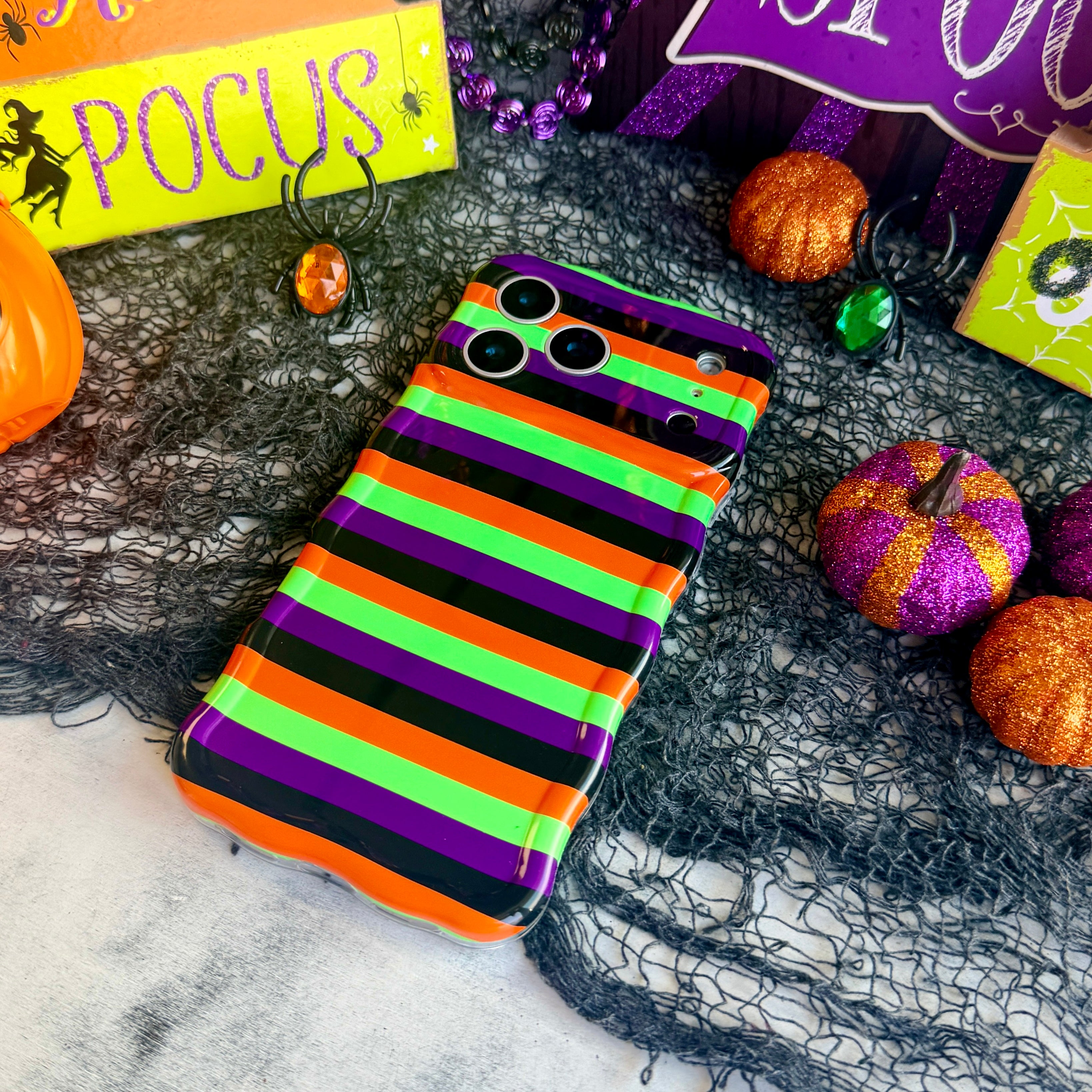Main Witch Energy Wavy Luxe MagSafe iPhone case laid flat on black spiderweb mesh with purple and orange glitter pumpkins.