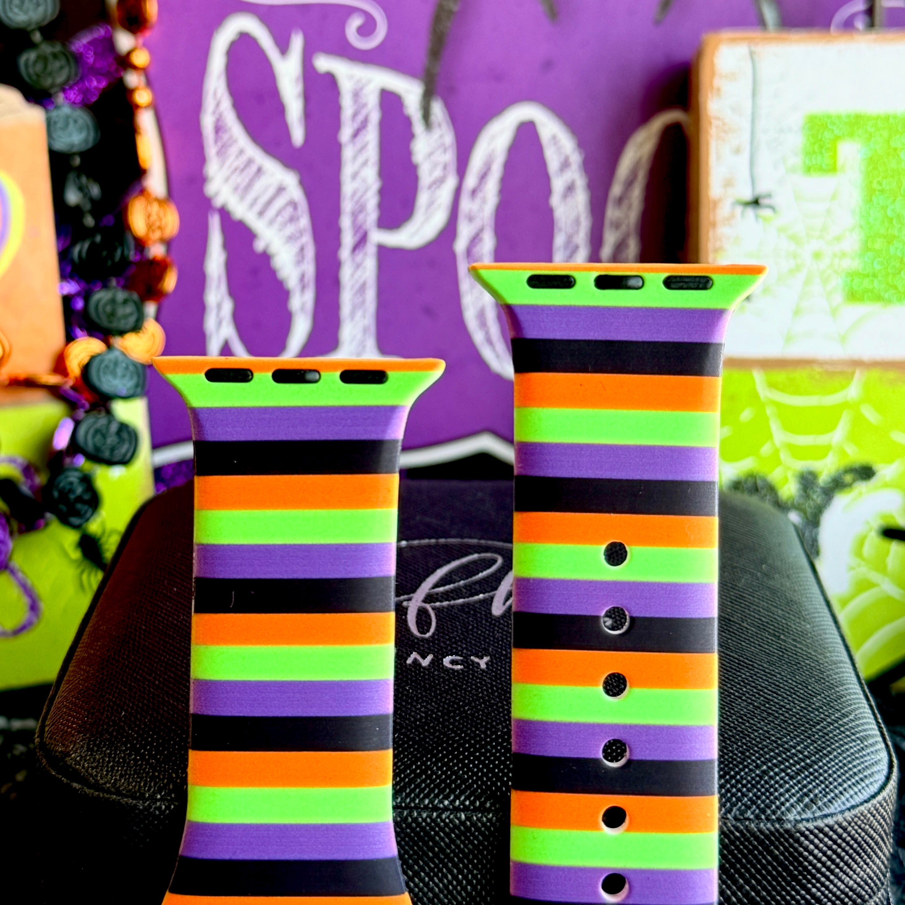 Both halves of the Main Witch Energy Apple Watch band standing upright against a purple SPOOKY sign with glitter pumpkins.