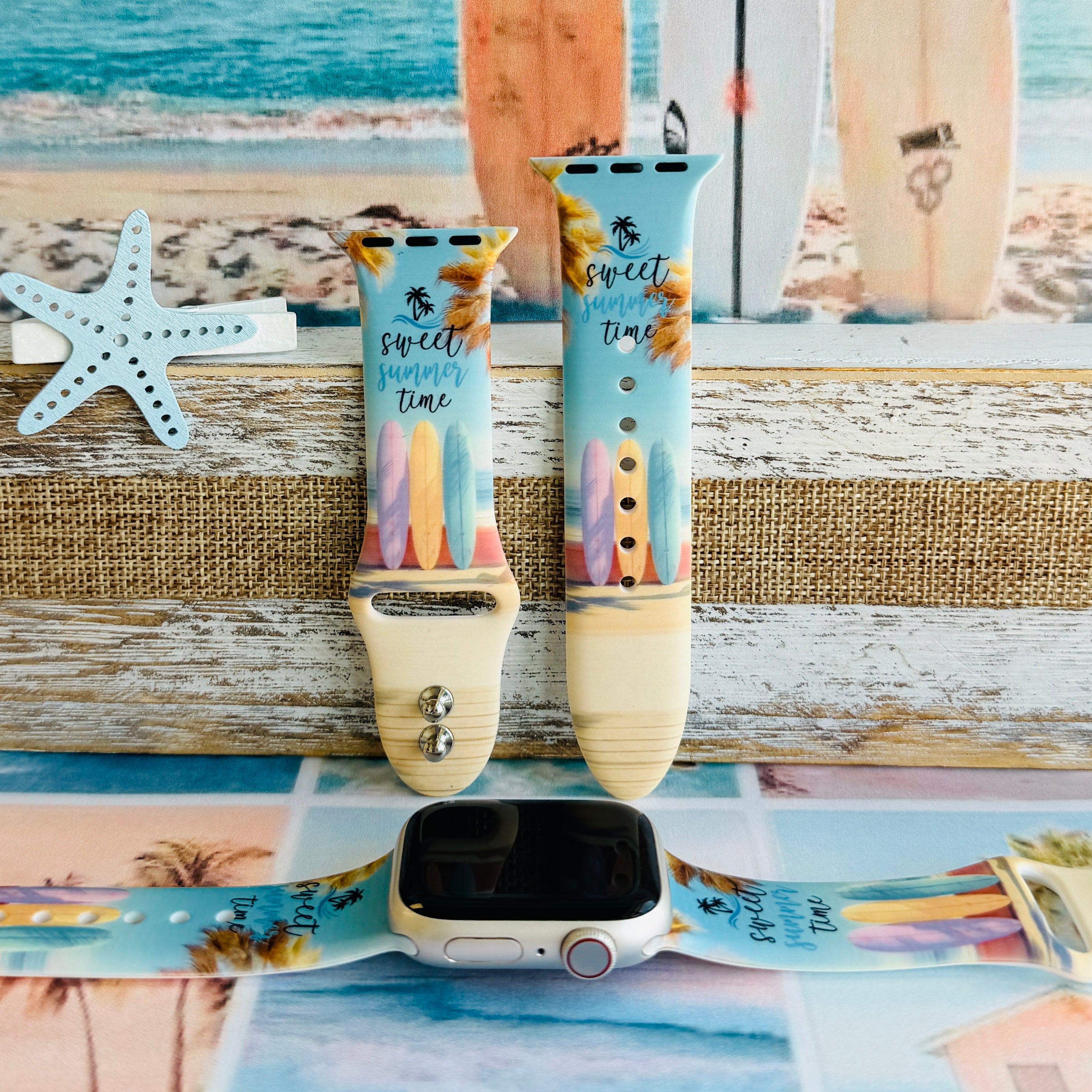 Sweet Summer silicone Apple Watch band with pastel pink, yellow, and blue surfboards, palm trees, and "sweet summer time" script on a soft watercolor beach scene, shown displayed and worn on Apple Watch against a coastal surfboard backdrop.