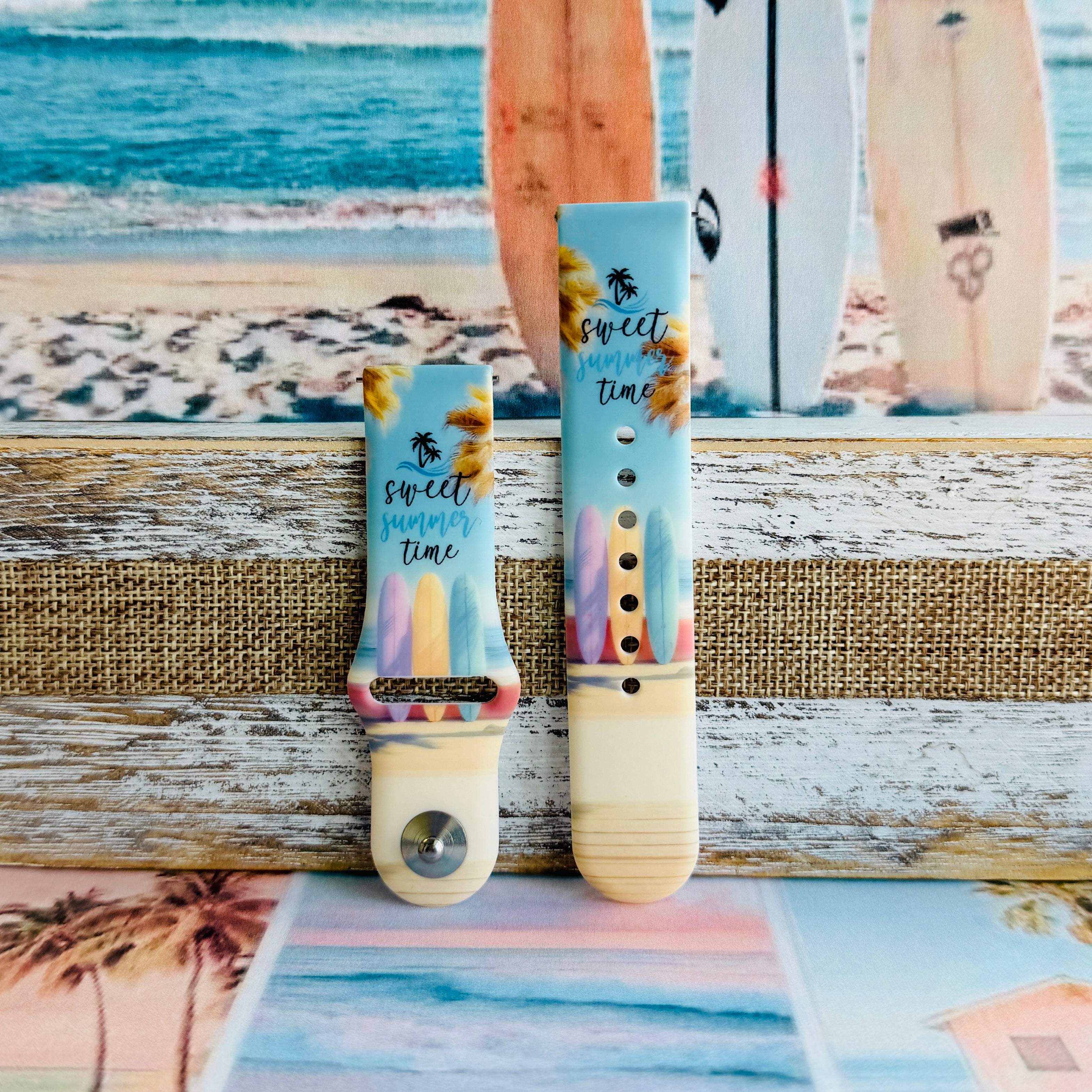 Sweet Summer silicone Samsung Galaxy Watch band with pastel pink, yellow, and blue surfboards, palm trees, and "sweet summer time" script on a soft watercolor beach scene, shown displayed and worn against a coastal surfboard backdrop.