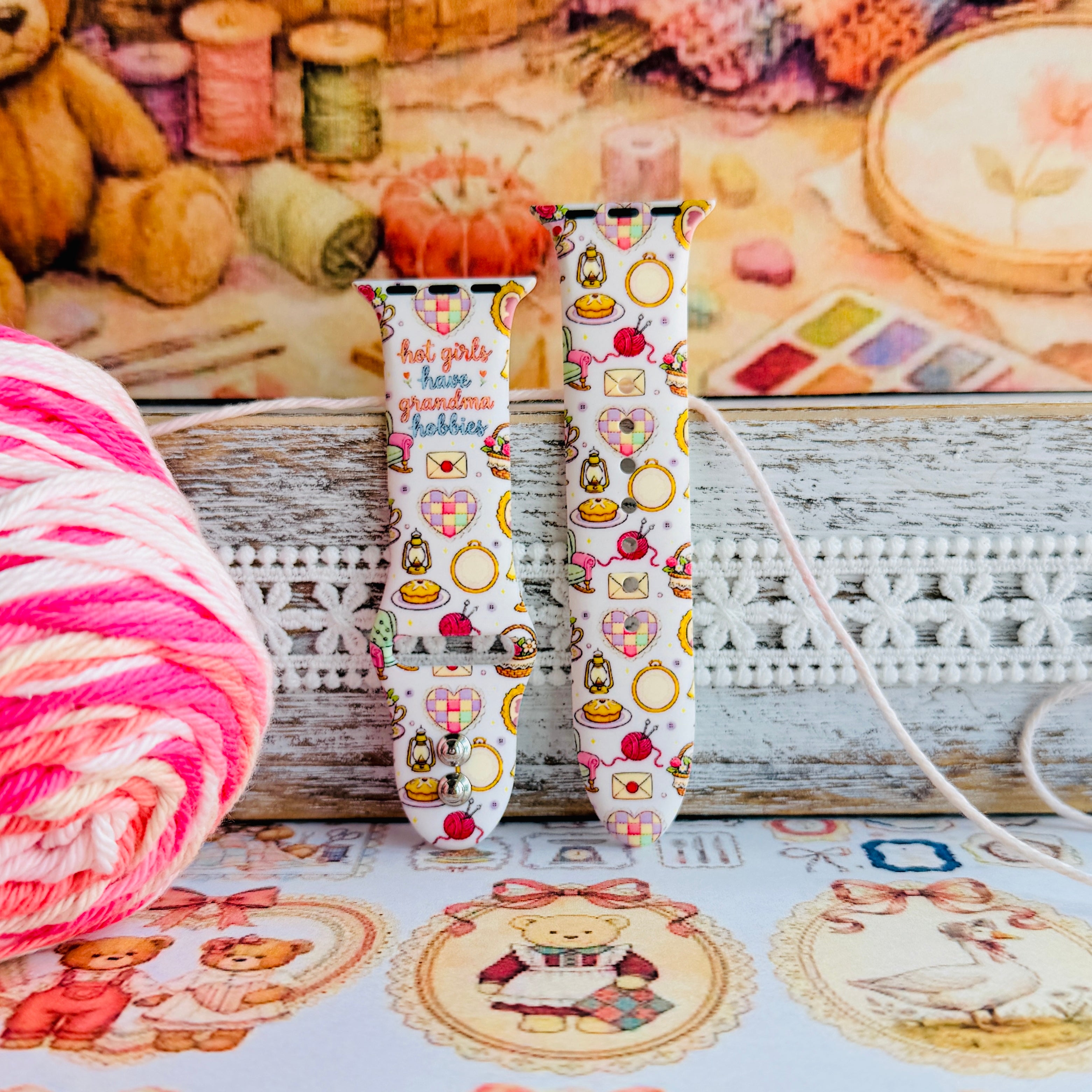 It's Giving Grandma Hobbies silicone Apple Watch band with "hot girls have grandma hobbies" script, patchwork hearts, yarn balls, knitting needles, embroidery hoops, lanterns, pies, and teacups on a cream base, shown displayed and worn on Apple Watch against a cottagecore craft backdrop.