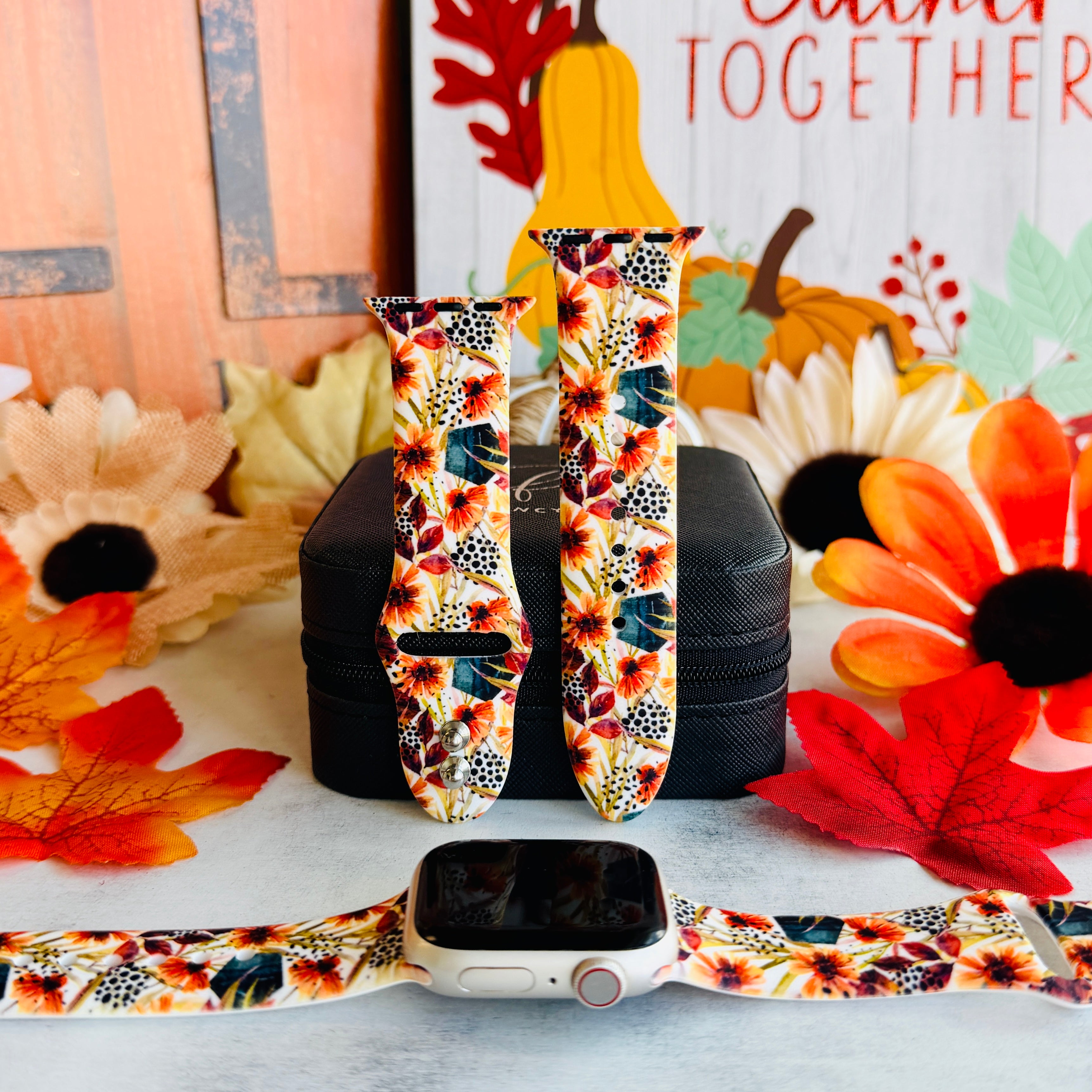 Sienna Petals silicone Apple Watch band shown in both sizes with an Apple Watch at the base, cream with burnt orange watercolor daisies and teal leaves.