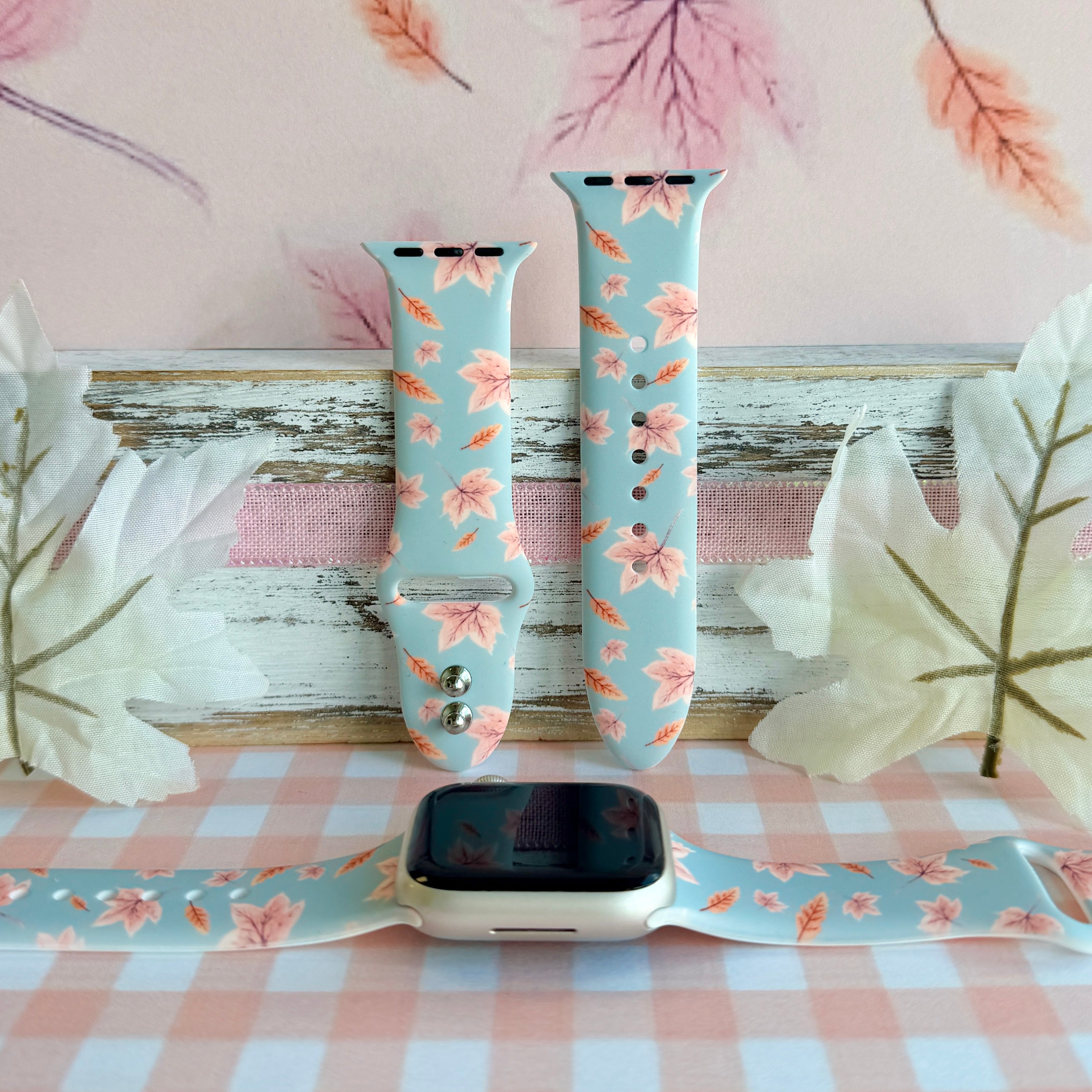 Autumn Breeze silicone Apple Watch band shown in both sizes with an Apple Watch at the base, dusty blue with blush maple leaves and coral wheat sprigs.