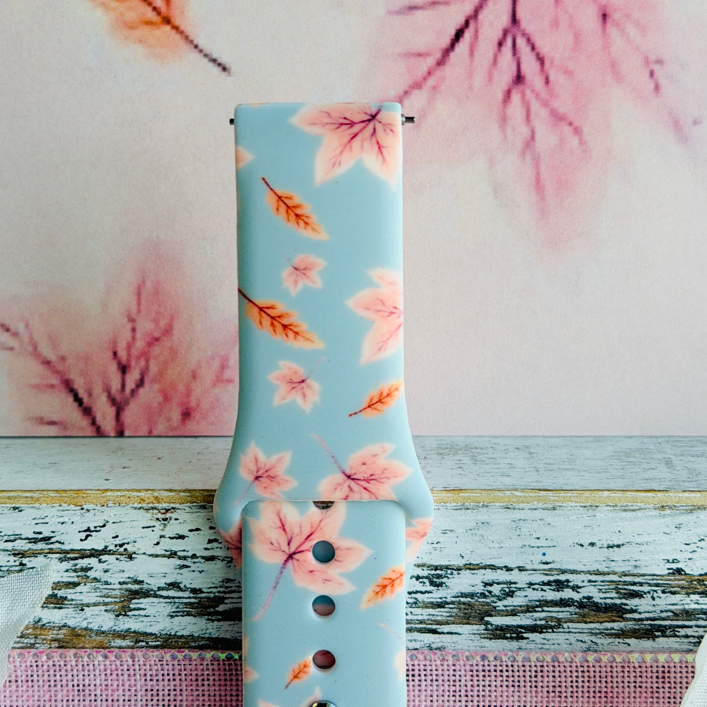 Close view of the Autumn Breeze Samsung Galaxy Watch band showing the soft blue silicone printed with blush pink maple leaves.