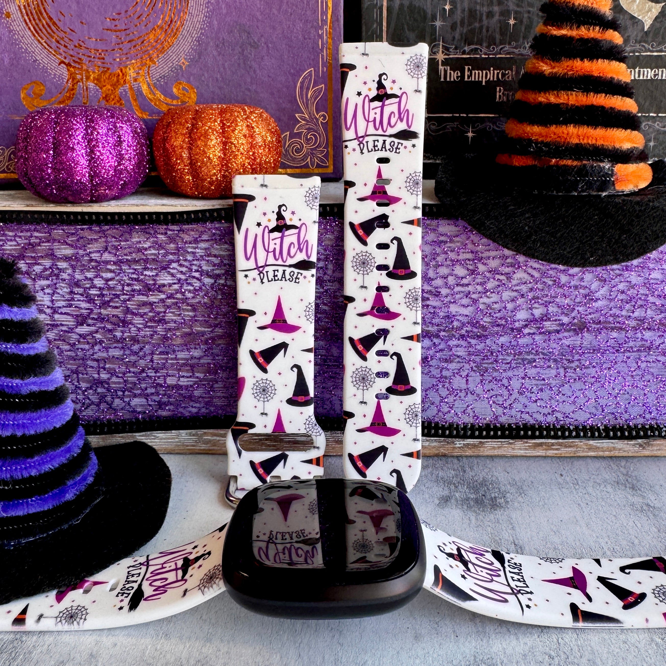 Witch Please silicone Fitbit Versa 3/4 and Sense band hero shot in cream with purple witch hats, shown with a black Fitbit Versa.