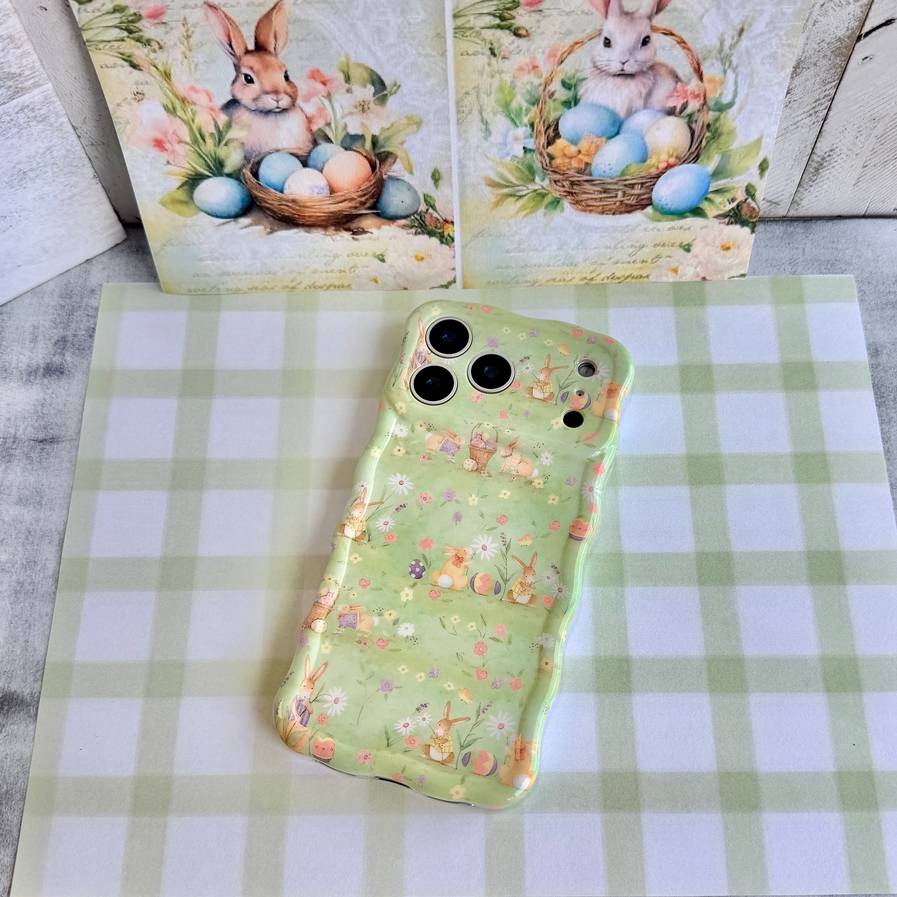 Sage green wavy iPhone case featuring a vintage watercolor pattern of bunnies, Easter eggs, and spring flowers.