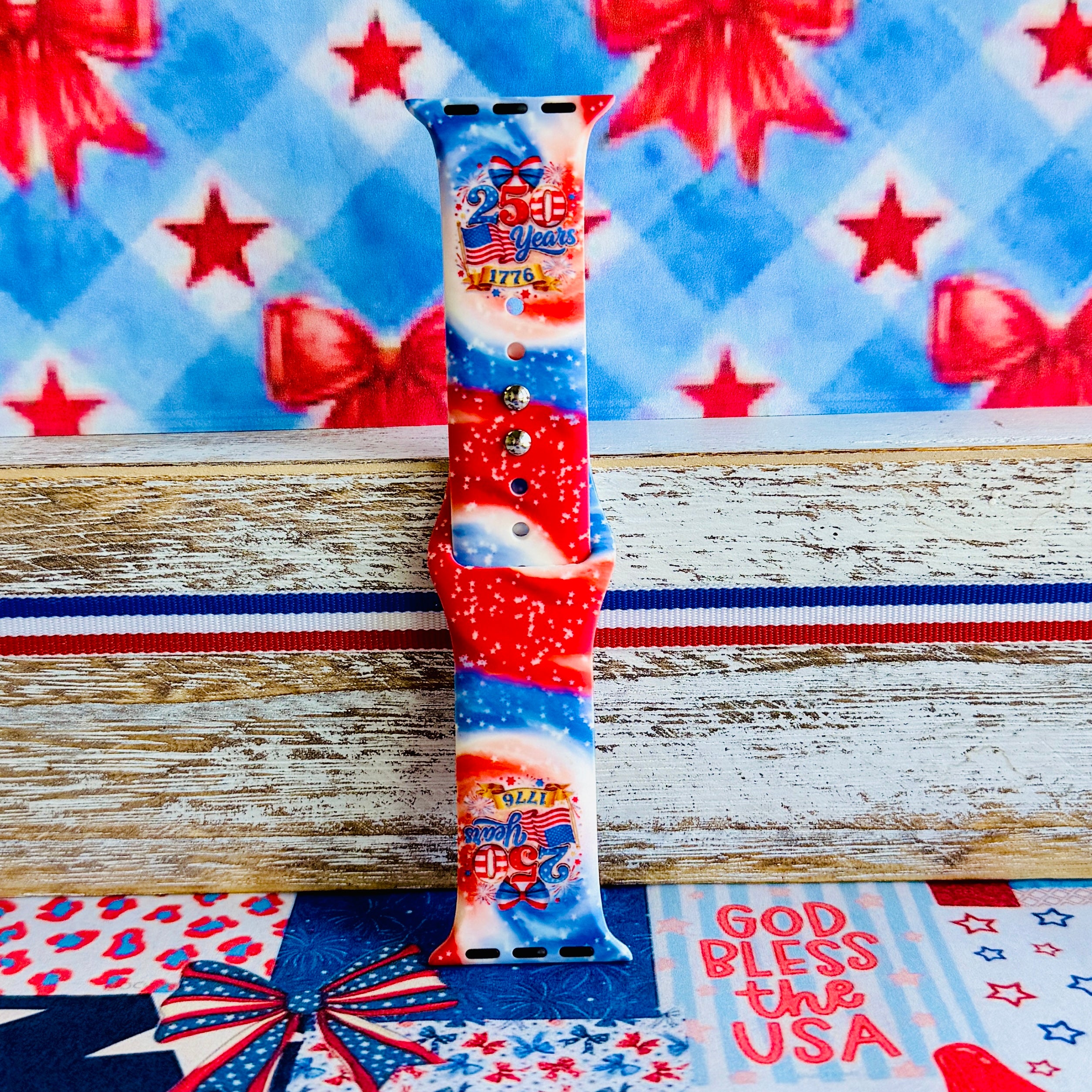 Sweet Freedom 250 silicone Apple Watch band celebrating America's 250th anniversary with "250 Years 1776" emblem, American flag, fireworks, red bow, and red, white, and blue tie-dye swirl with star sparkle, shown displayed and worn on Apple Watch against a patriotic 4th of July backdrop.