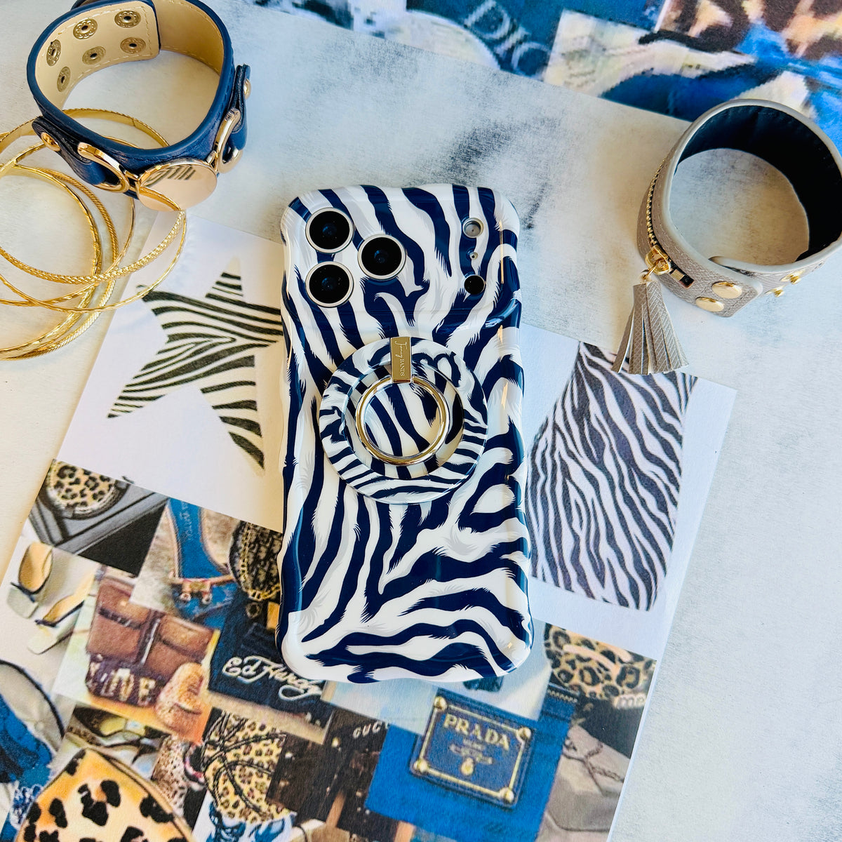 The Zebra, Obviously navy and white zebra MagSafe grip ring attached to the matching zebra iPhone case, styled with gold bangles and a studded cuff on a fashion collage.