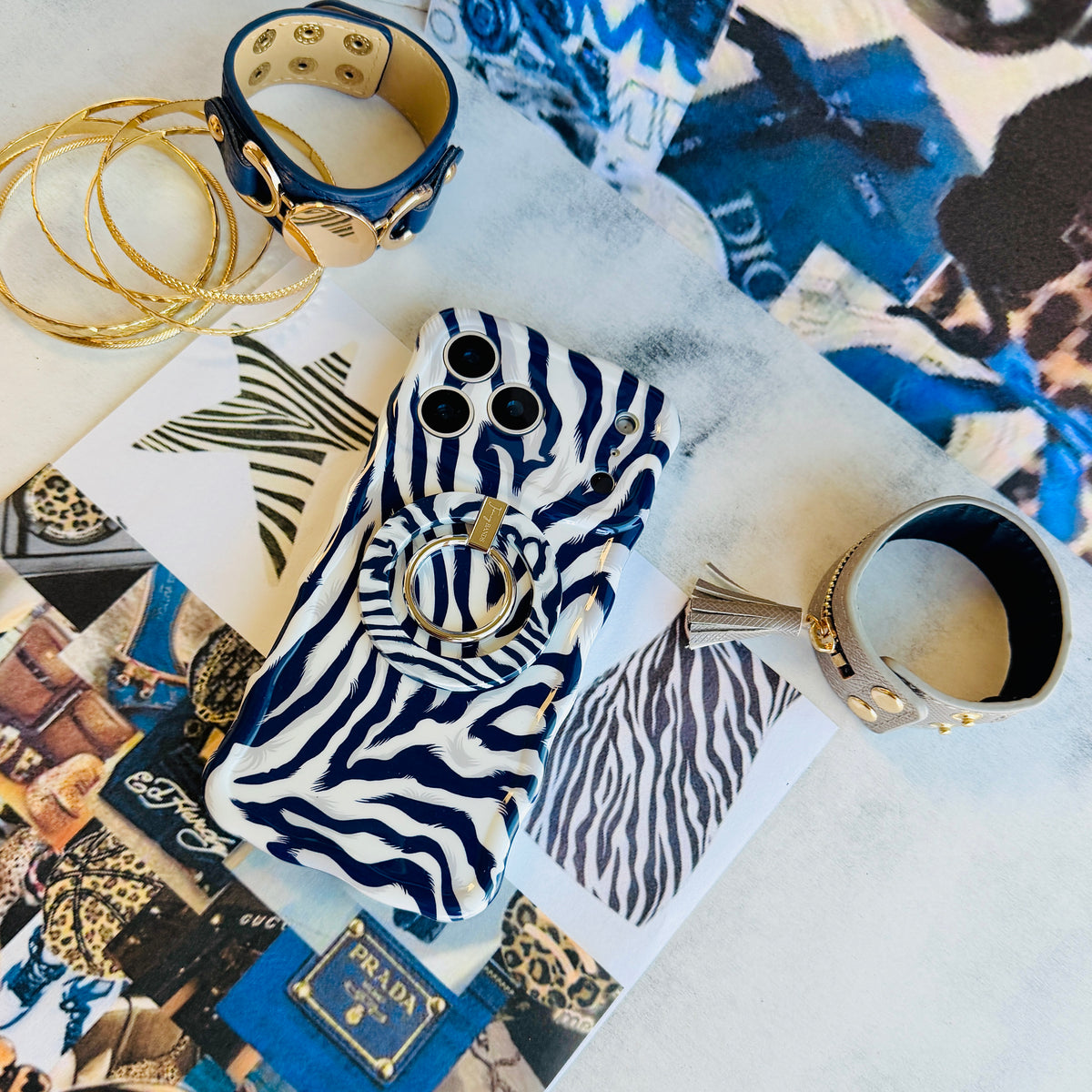 Zebra, Obviously navy zebra print iPhone case wearing the matching navy and white zebra MagSafe grip ring, styled on a designer fashion collage with gold hoops and a studded cuff.