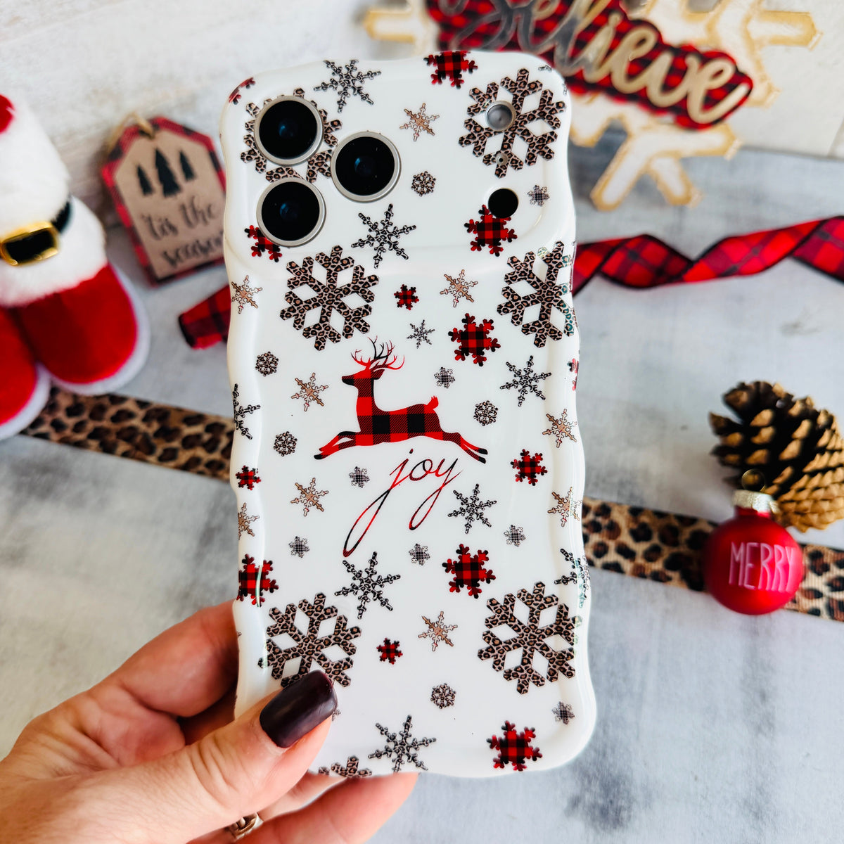 Hand holding the Deer Joy Wavy Luxe MagSafe iPhone case, buffalo-plaid reindeer and snowflakes on white
