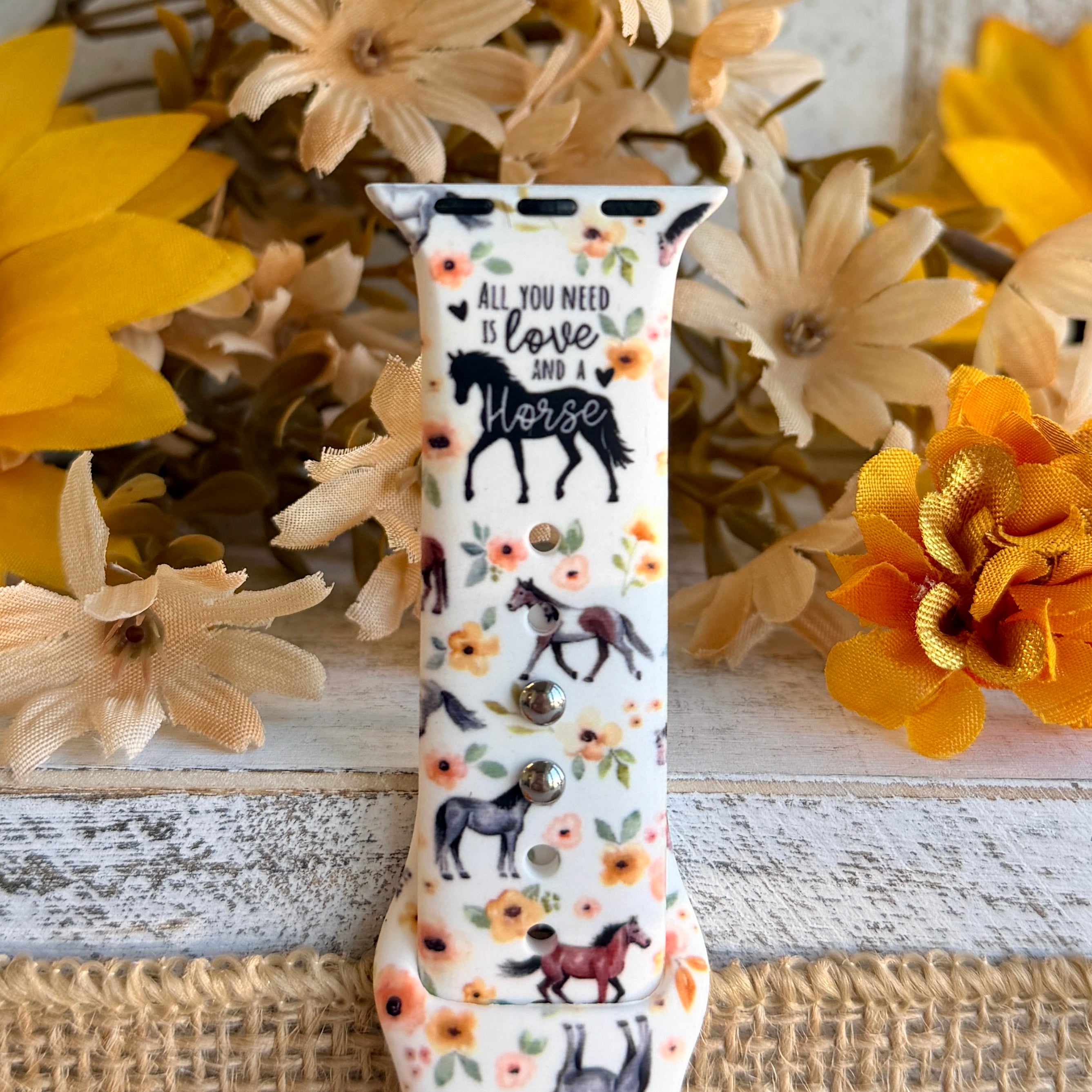 Decorative watch strap with horse design and floral patterns on a wooden surface with flowers.