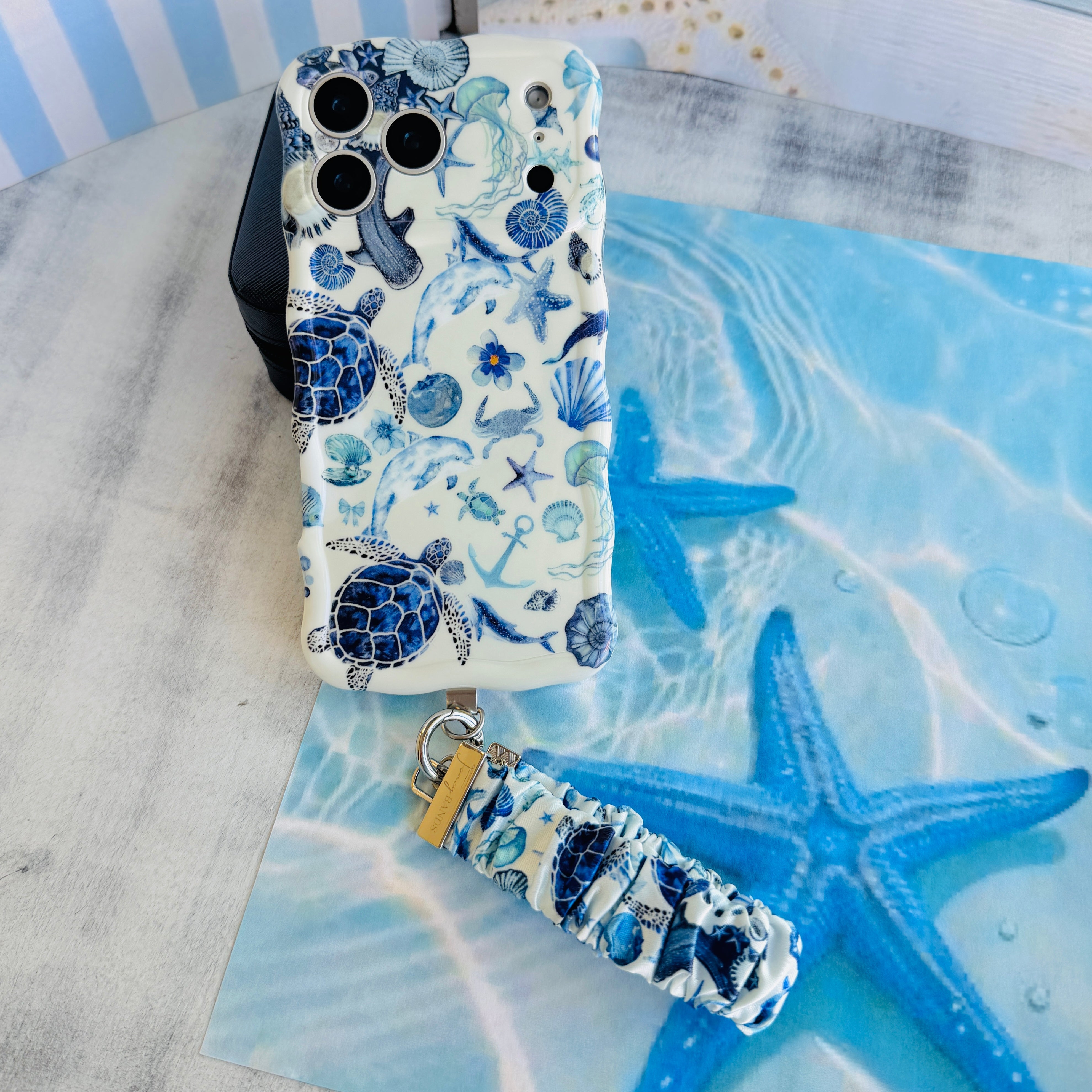Blue Lagoon scrunchie phone wrist strap clipped to the matching Blue Lagoon Wavy Luxe iPhone case