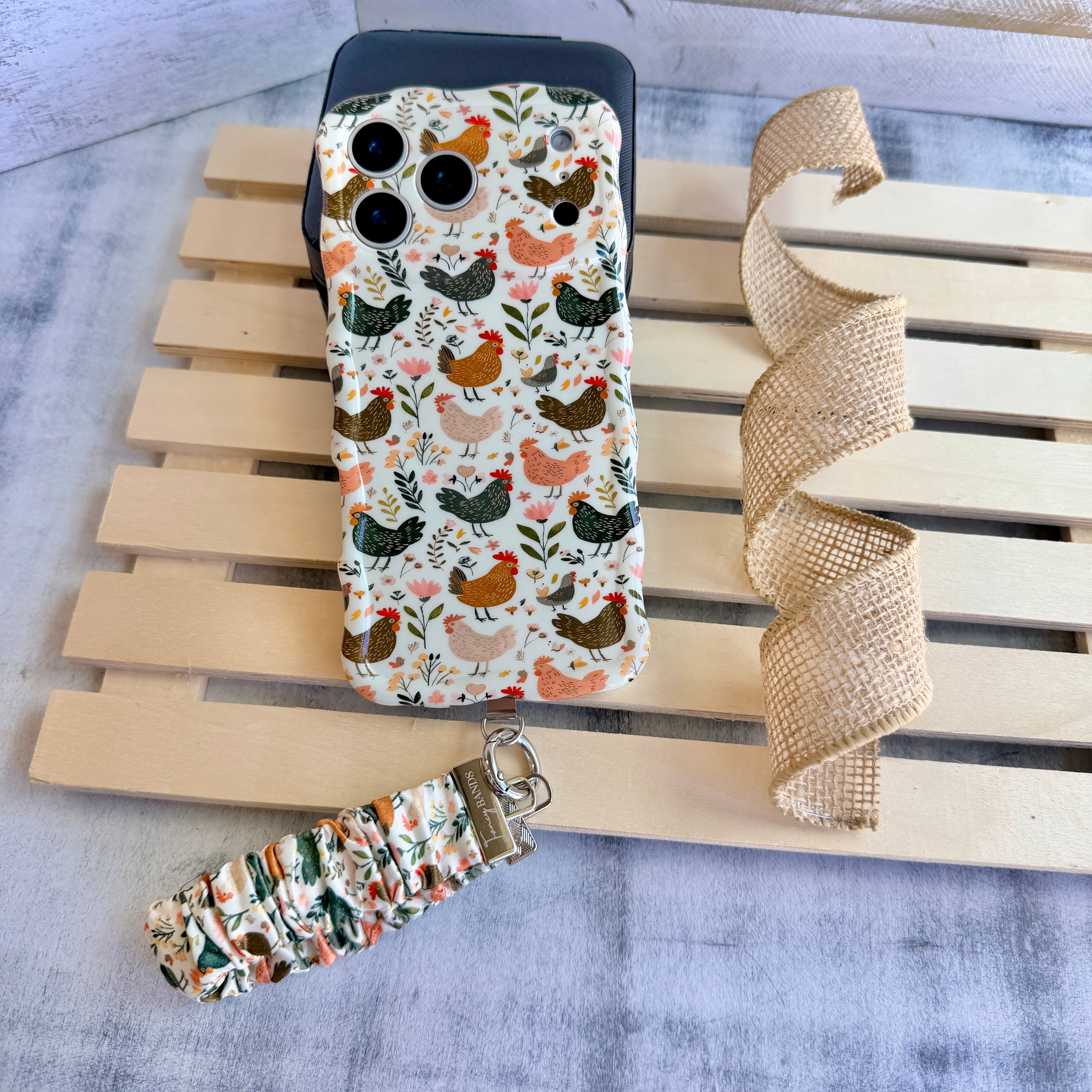 Cluckin' Cute scrunchie phone wrist strap clipped to the matching Cluckin' Cute Wavy Luxe iPhone case