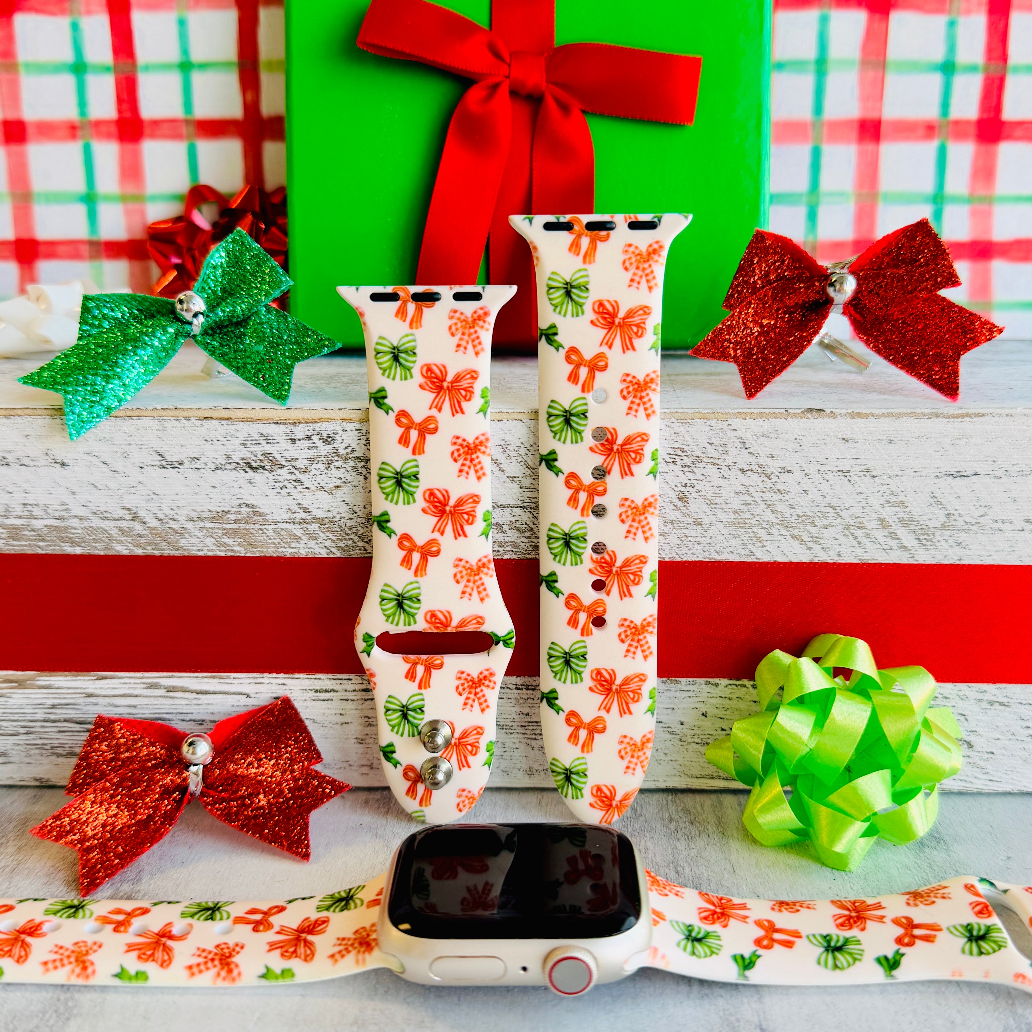 Jingle Bows Apple Watch band with red, orange, and green ribbon bows on cream background styled with wrapped Christmas presents