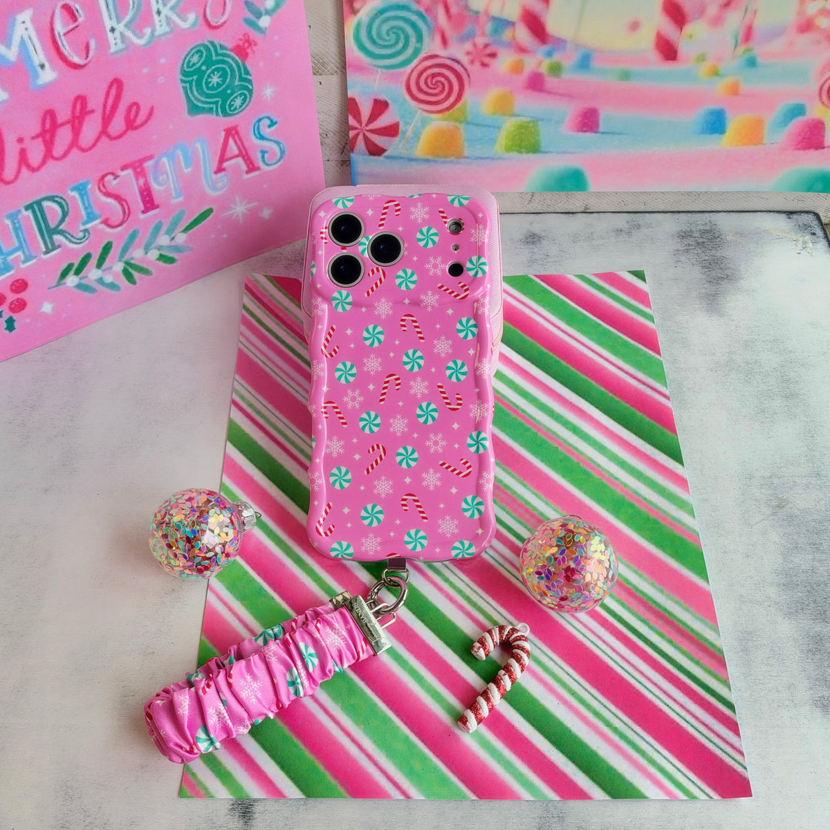 Peppermint Cutie iPhone case with the matching scrunchie phone wrist strap attached, laid flat with a mini candy cane