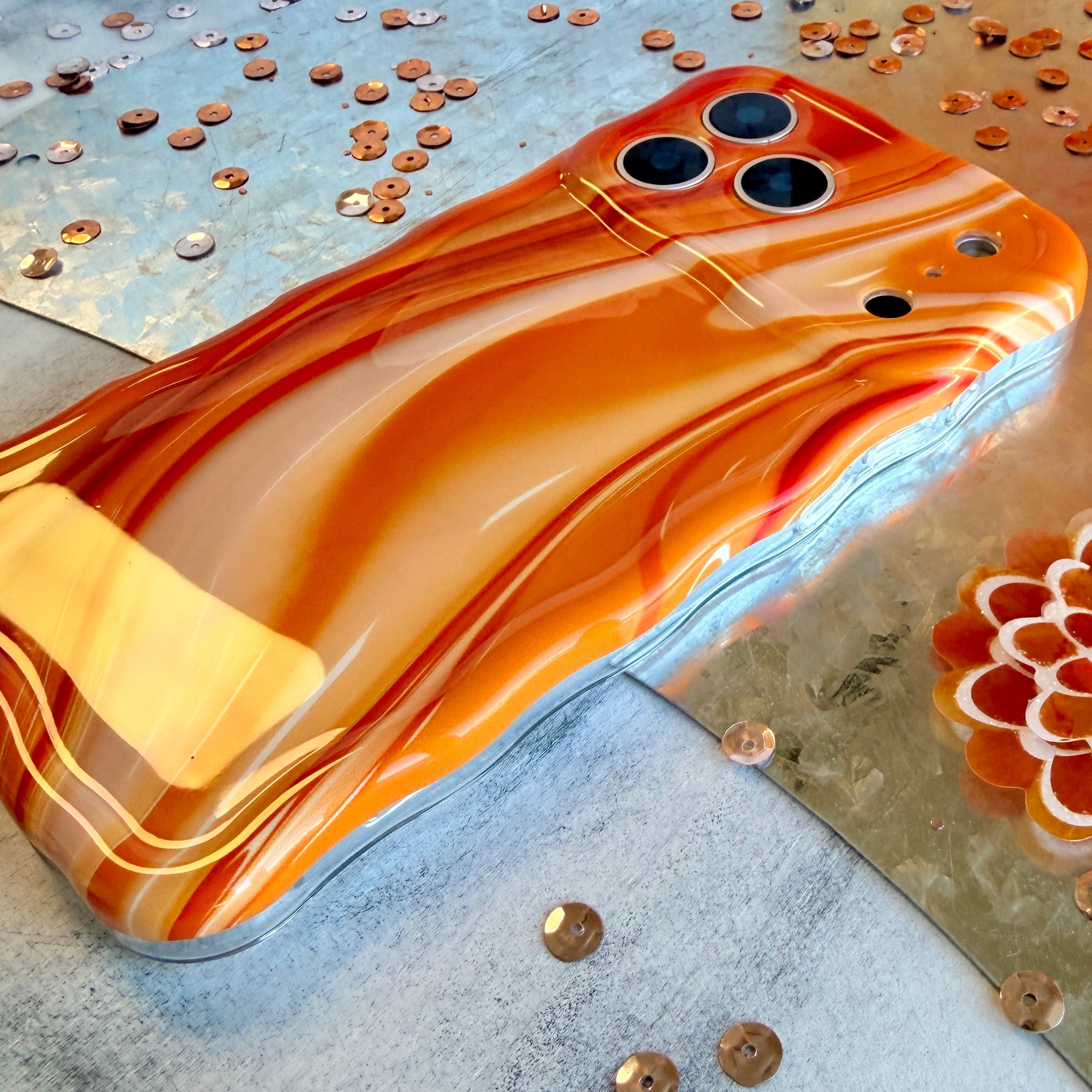 Orange and gold phone case on a textured surface with coins