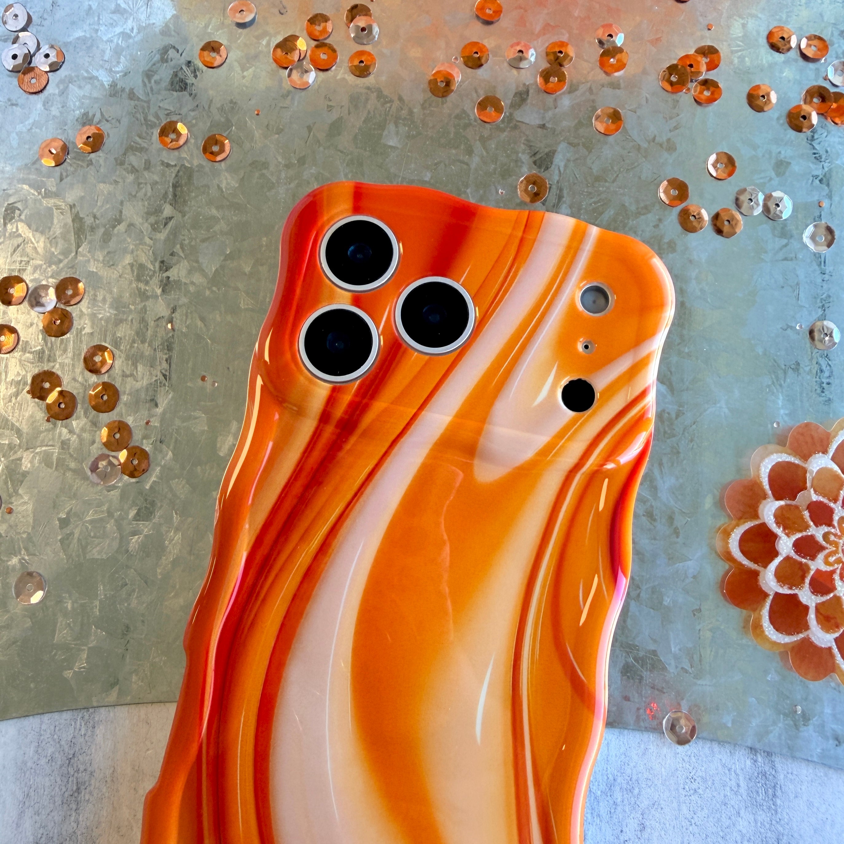 Decorative orange iphone case with orange and white swirl pattern on a textured surface.