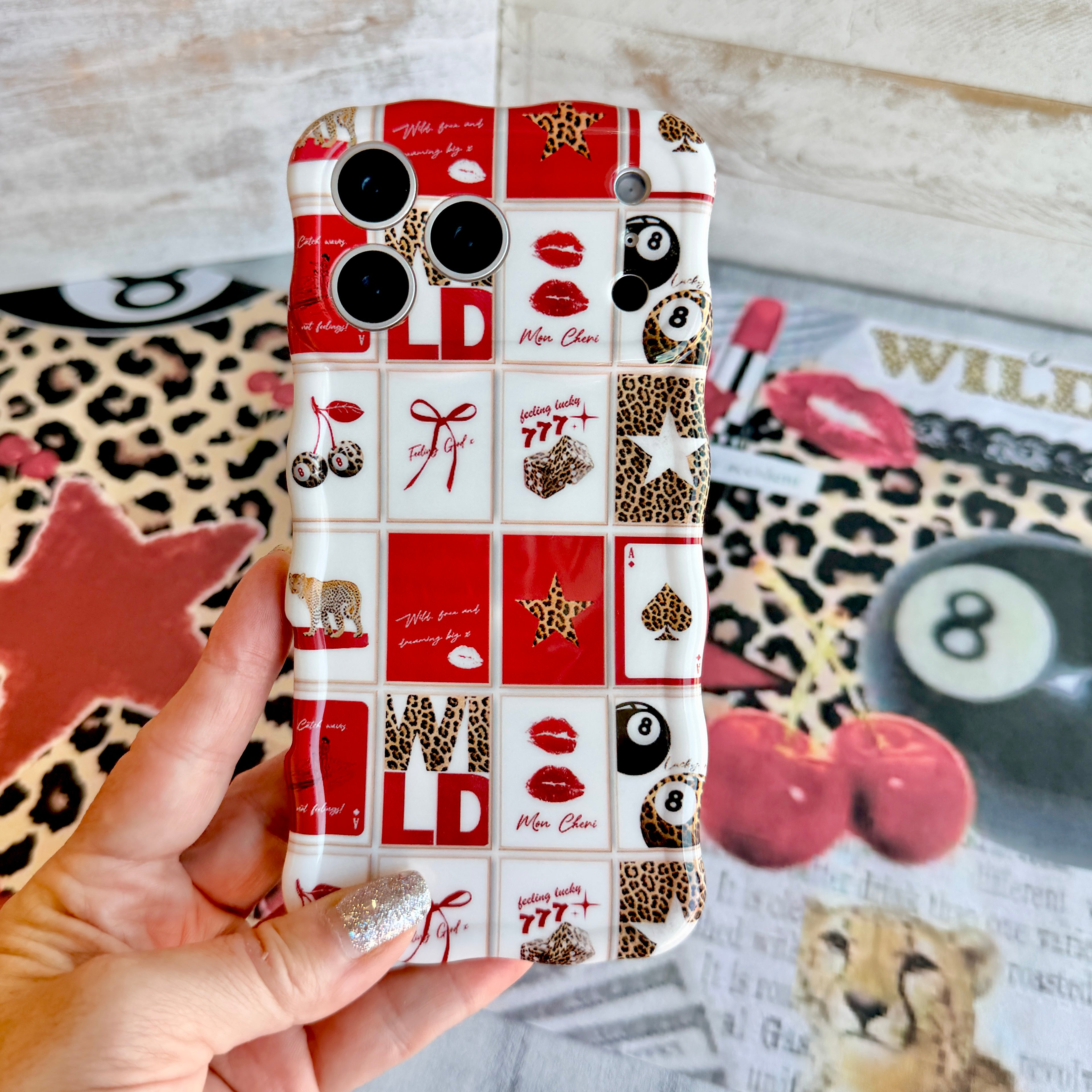 Trendy red and white wavy iPhone case featuring a collage of leopard print cherries, 8-balls, red lips, and lucky 777 dice with a high-gloss finish.