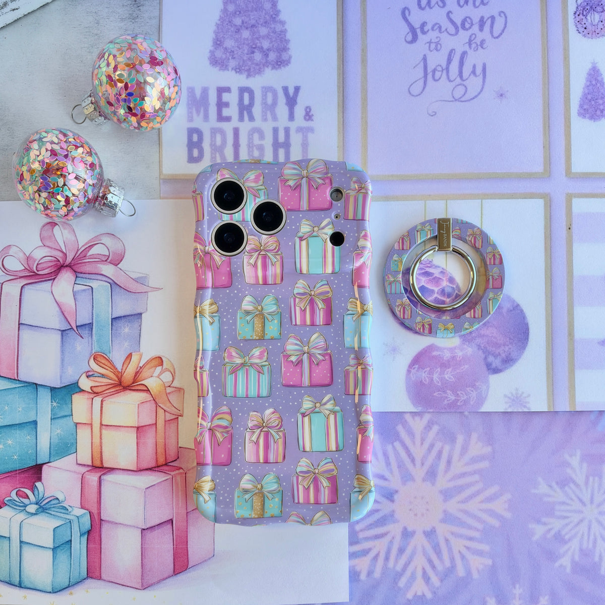 No Peeking, Darling MagSafe grip ring lying beside the matching pastel present iPhone case and a stack of wrapped gifts