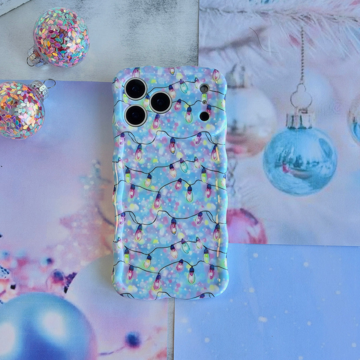 Twinkle All The Way iPhone case lying flat beside a hanging blue glass ornament and glitter baubles