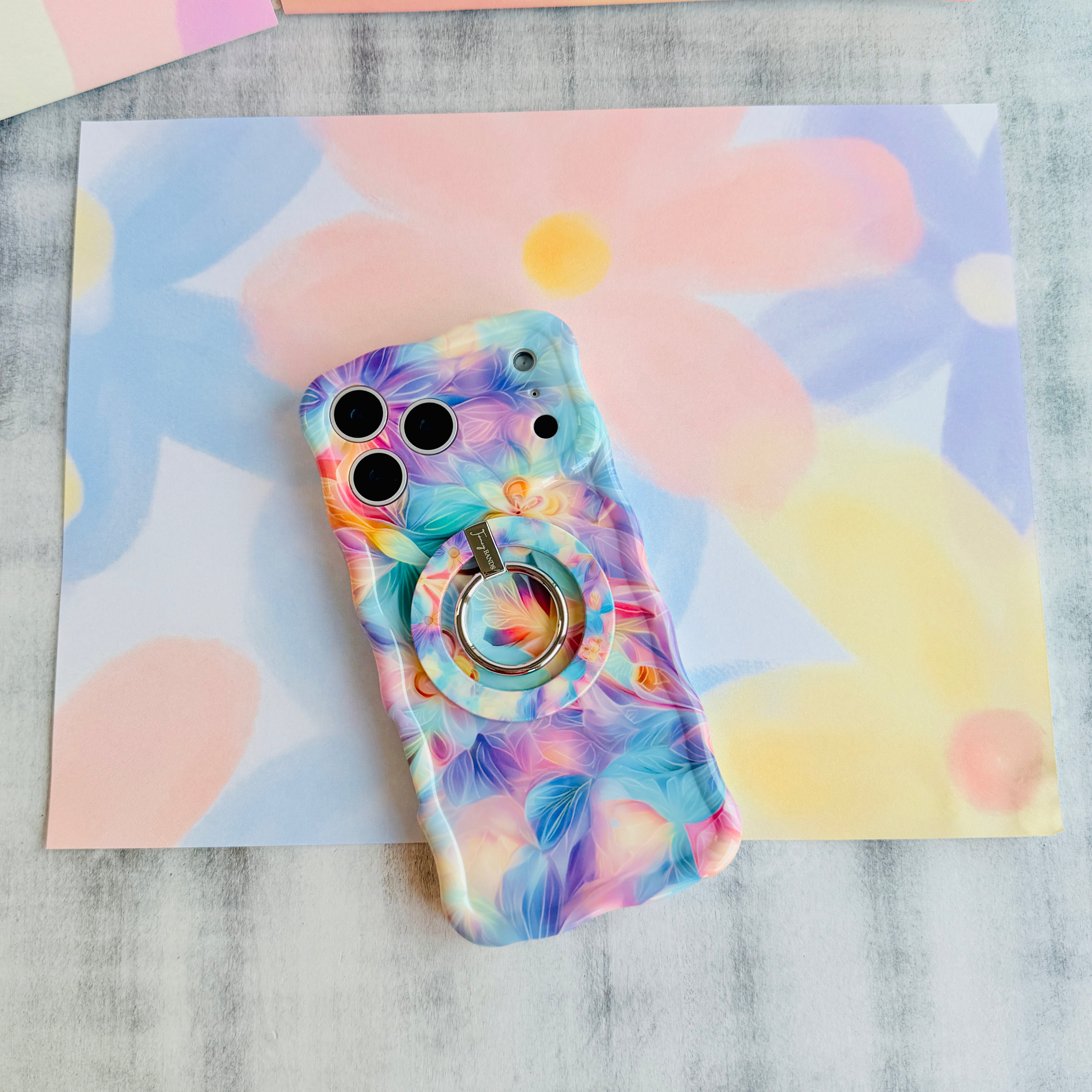 Trendy wavy iPhone case featuring an iridescent swirly pattern in pastel pink, blue, yellow, and lavender with a high-gloss finish.