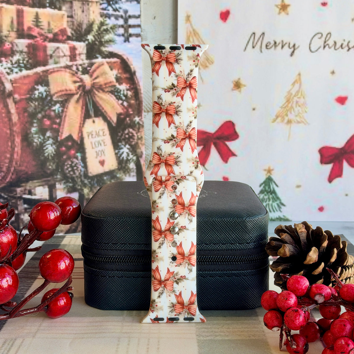 Deck Yourself in Bows & Holly Apple Watch band buckled and standing on a black jewelry box between red berries and a pinecone