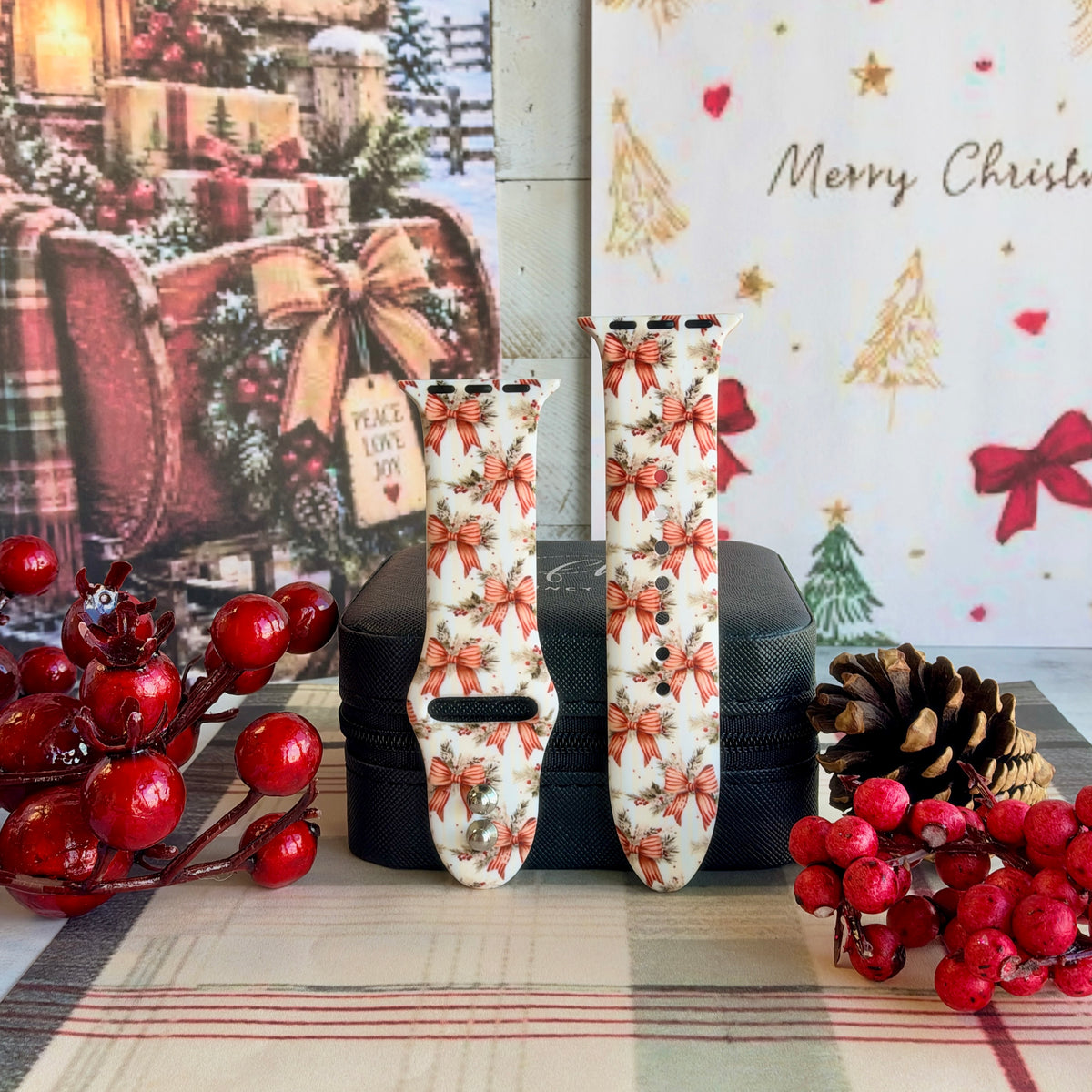 Both straps of the Deck Yourself in Bows & Holly silicone Apple Watch band on a black jewelry box with red berries and a pinecone