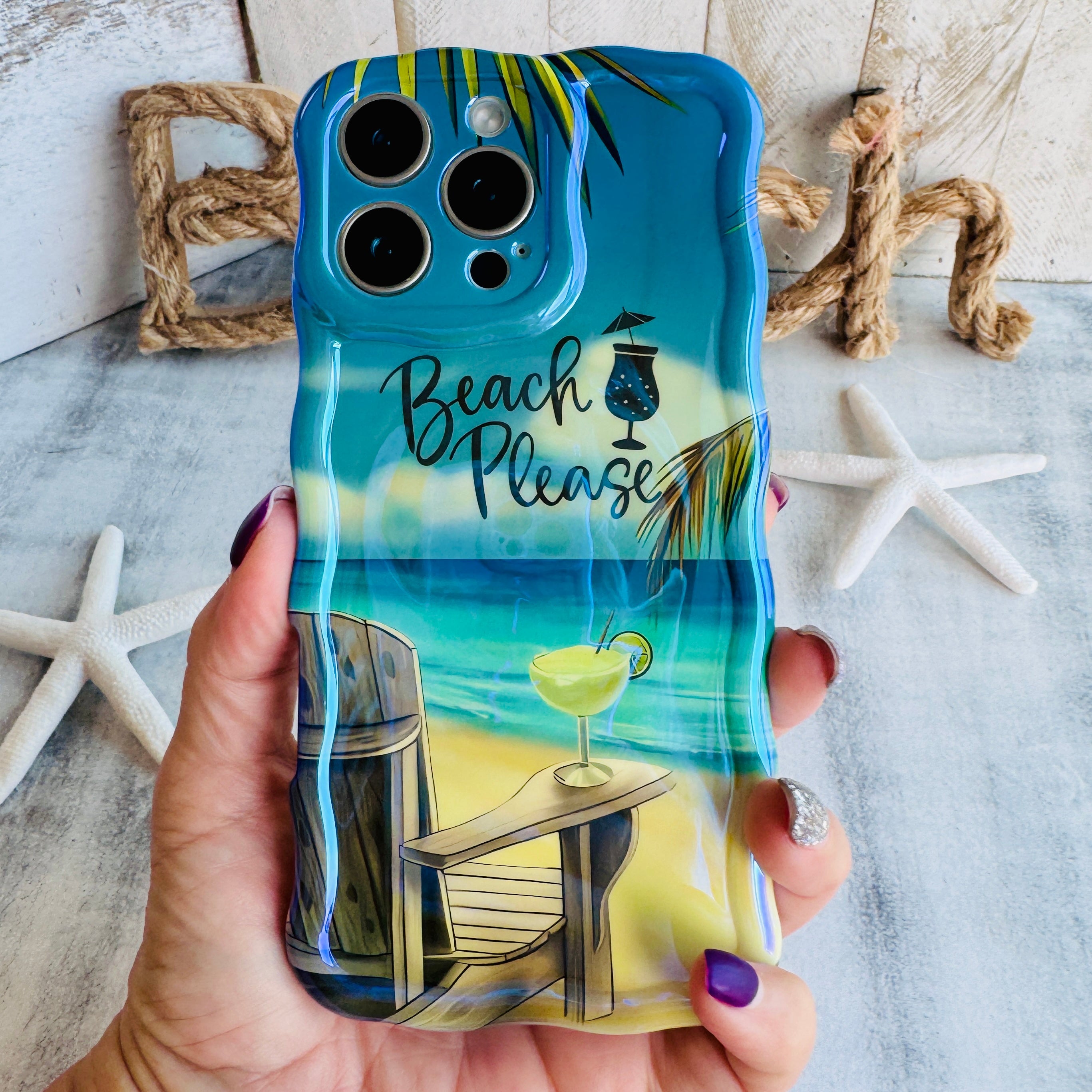Hand holding the Beach Please Wavy Luxe MagSafe iPhone case with a painted beach scene and hand-lettered Beach Please script