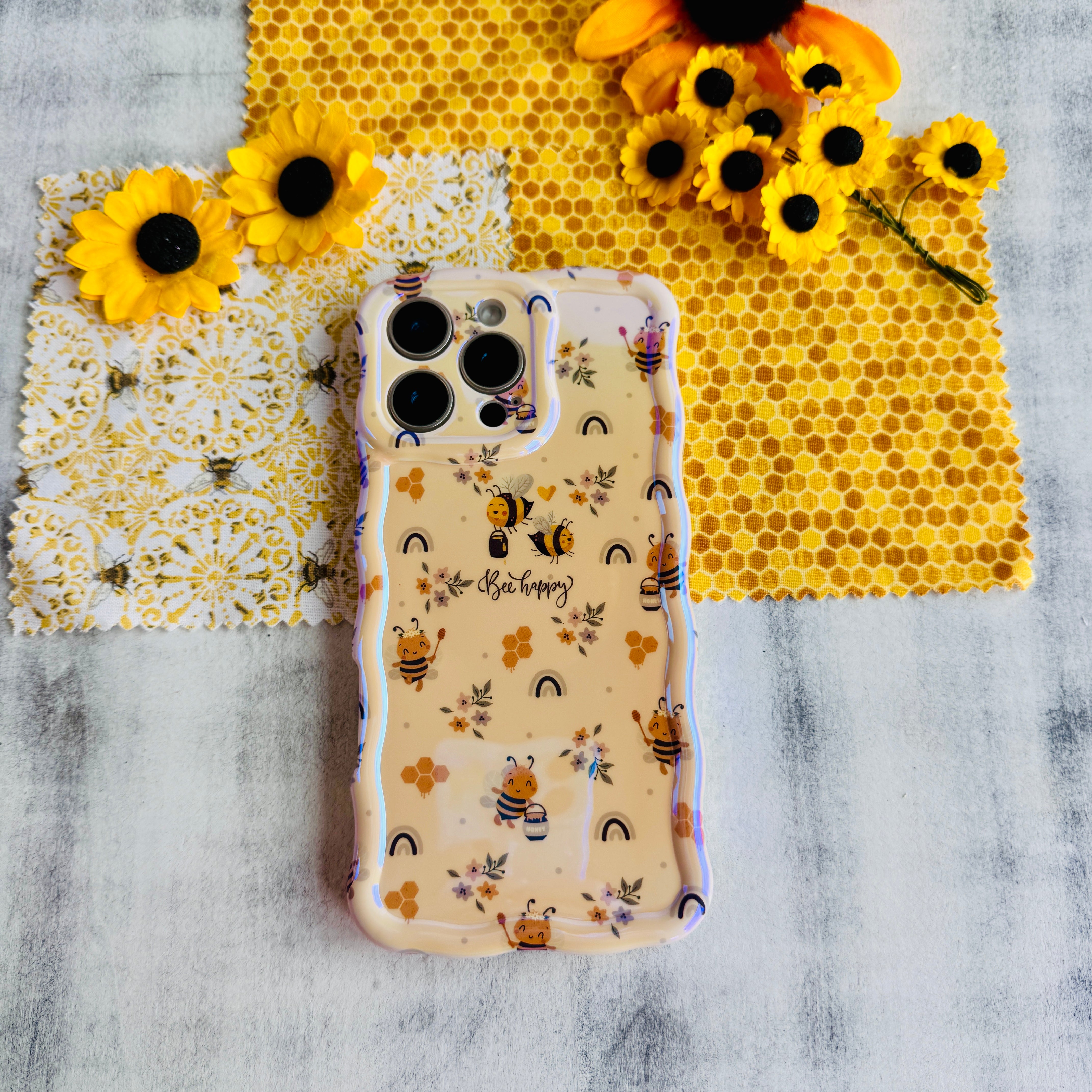 A phone case with a wavy edge design featuring floral prints and bees, held in a person's hand.