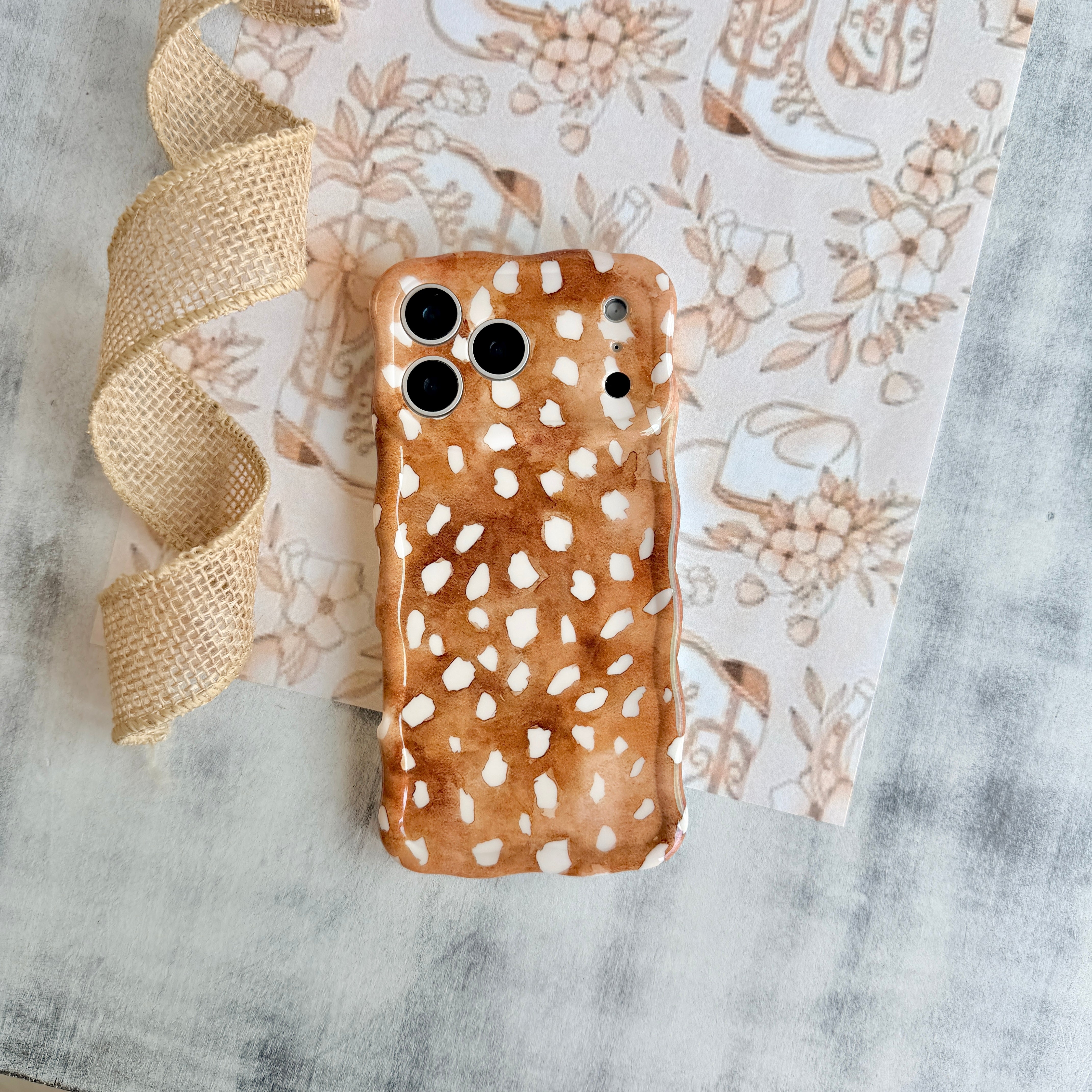 Warm whiskey-brown wavy iPhone case featuring a white fawn-spotted pattern with a high-gloss finish.