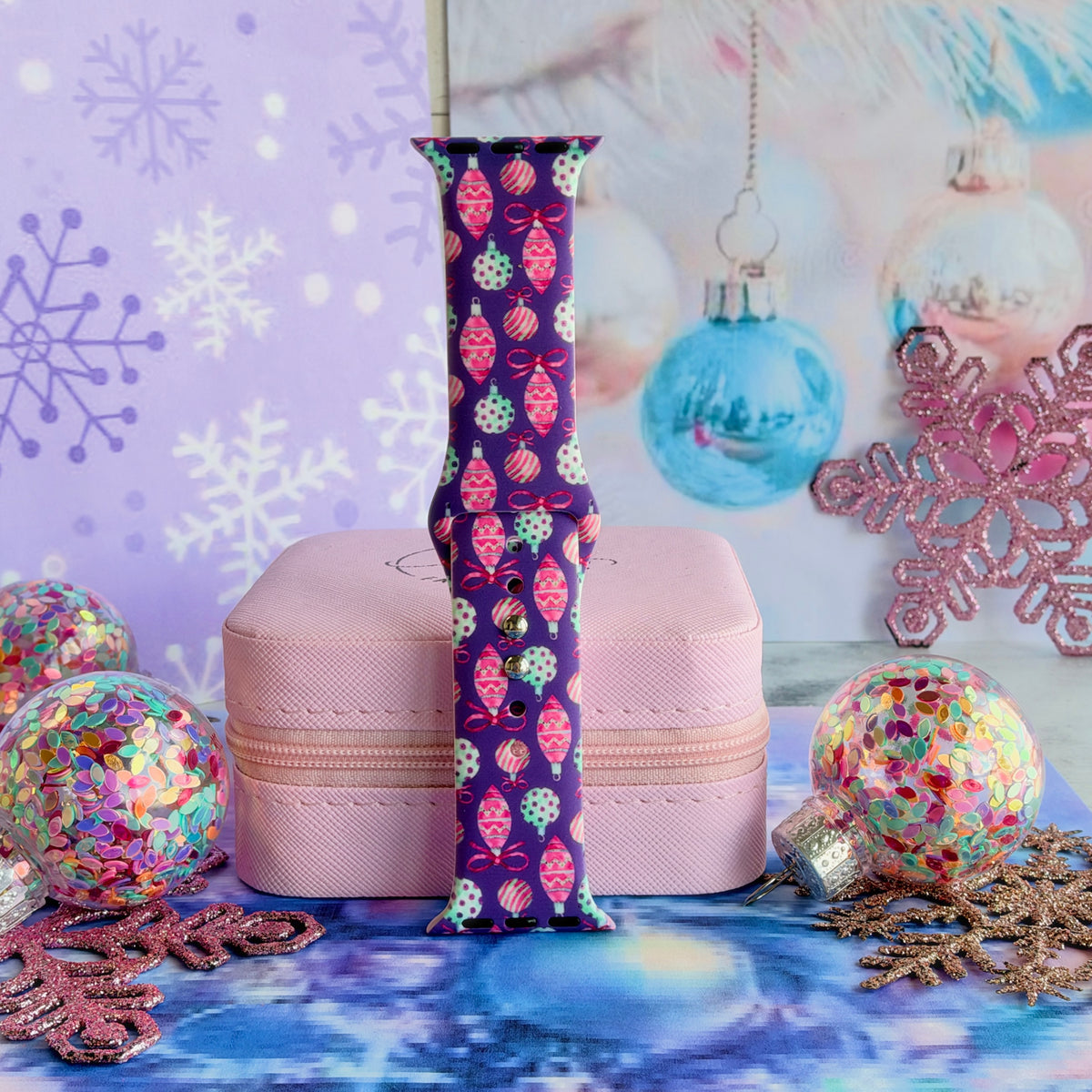 Single Just One More Ornament Apple Watch band strap standing on a pink jewelry box with aqua and pink glass ornaments behind