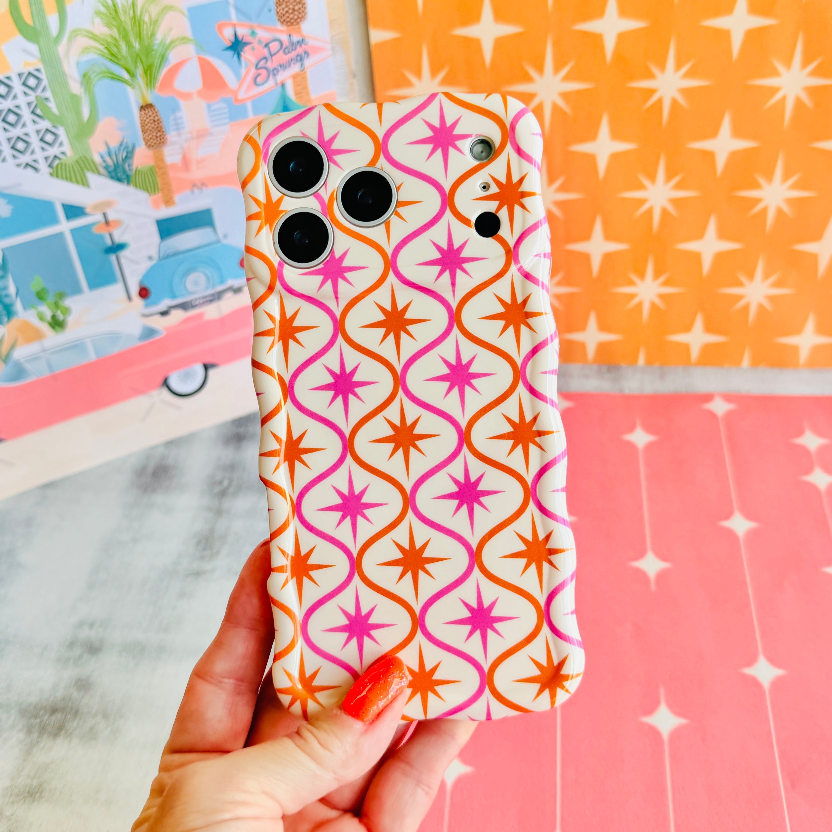 Trendy wavy iPhone case featuring a pink and orange starburst geometric pattern on a cream background with a high-gloss finish.